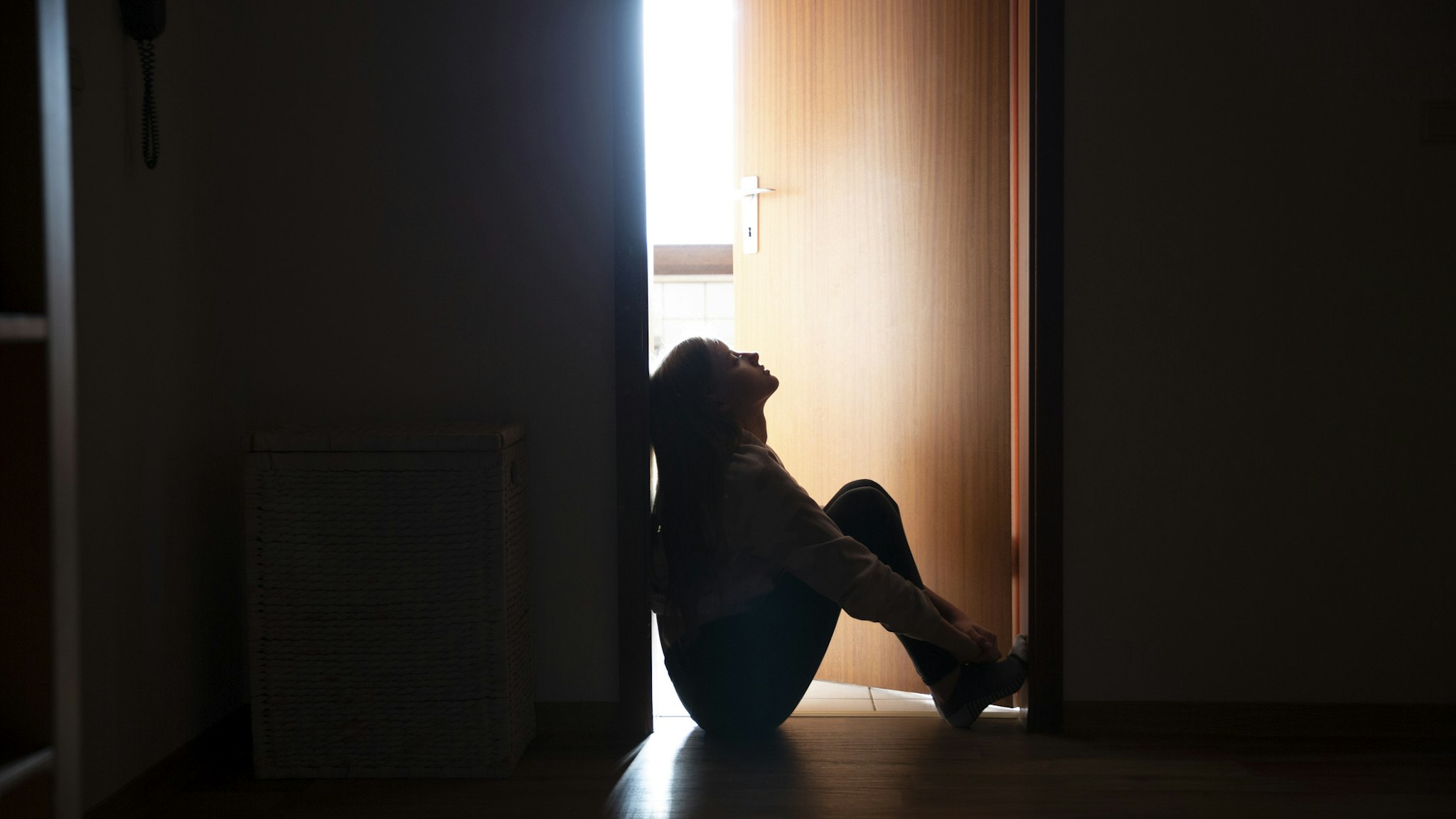 Backlit teenager sitting in a dark indoor doorway in contemplation - stock photo