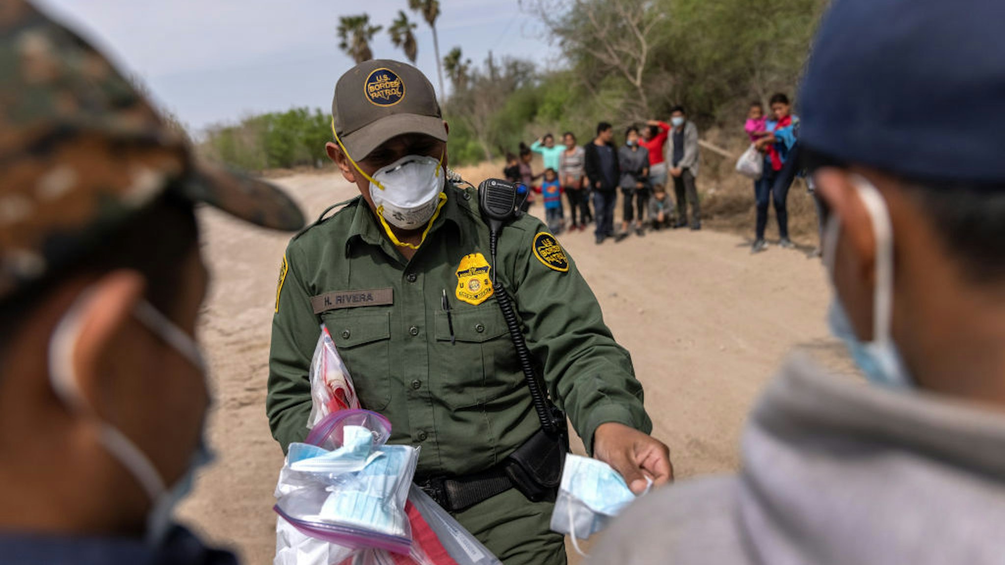HIDALGO, TEXAS - MARCH 25: A U.S. Border Patrol agent hands out masks to unaccompanied minors after a group of asylum seekers crossed the-Rio Grande into Texas on March 25, 2021 in Hidalgo, Texas. A large group of families and unaccompanied minors, mostly teenagers, came across the border onto private property, where Border Patrol agents took aside the unaccompanied minors for separate transport. The Biden administration is permitting minors to stay in the U.S., whereas many families, especially with older children, are being deported. (Photo by John Moore/Getty Images)