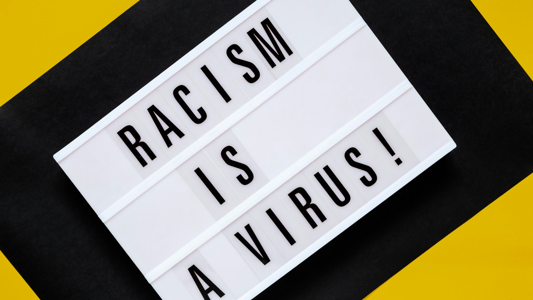 Racism is a Virus - conceptual text on light board on yellow ang black background - stock photo