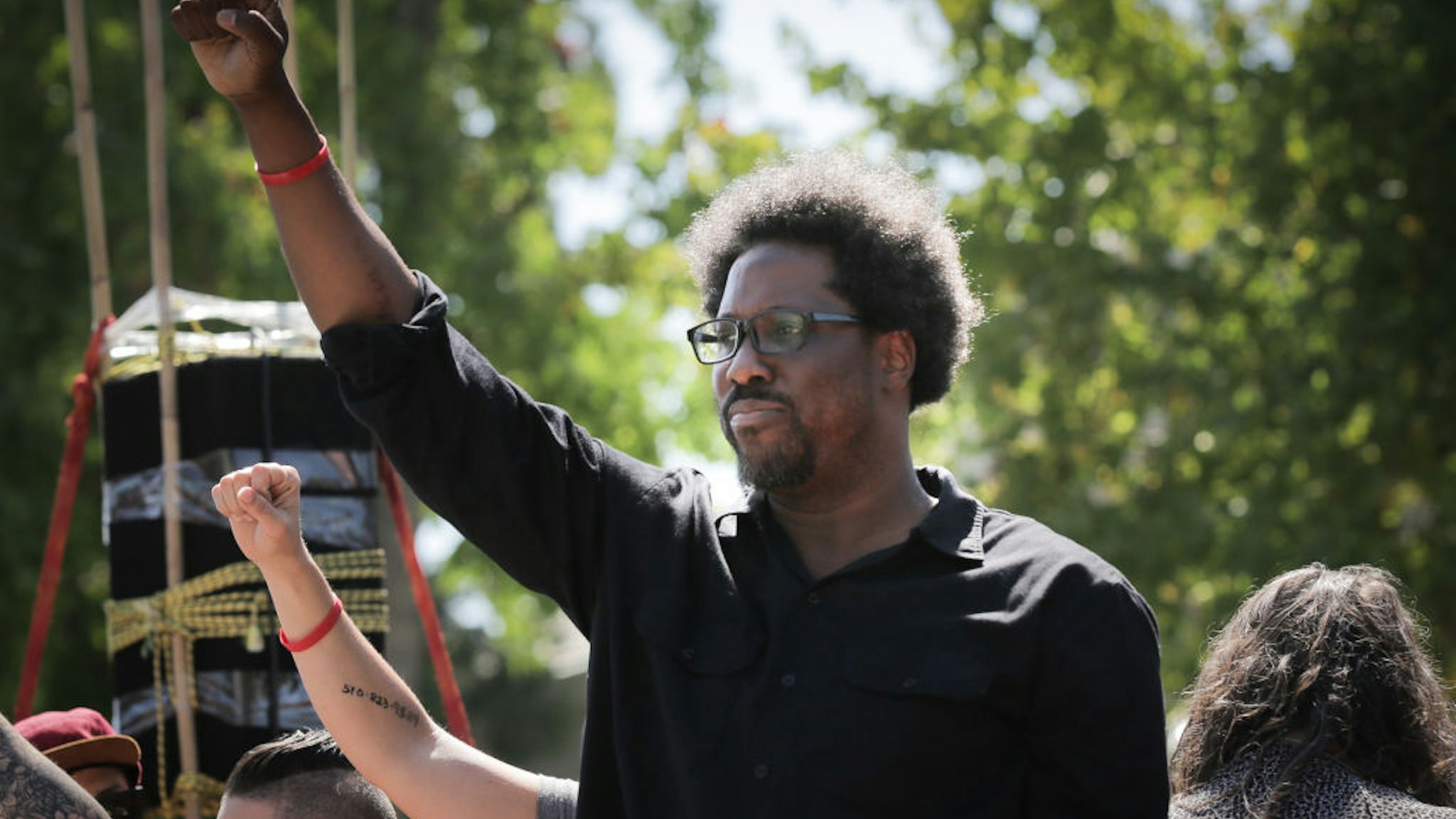 BERKELEY, CA - AUGUST 27: Comedian W. Kamau Bell raises his fist from a truck as people begin to march from MLK Jr. Park on August 27, 2017 in Berkeley, California. (Photo by Elijah Nouvelage/Getty Images)