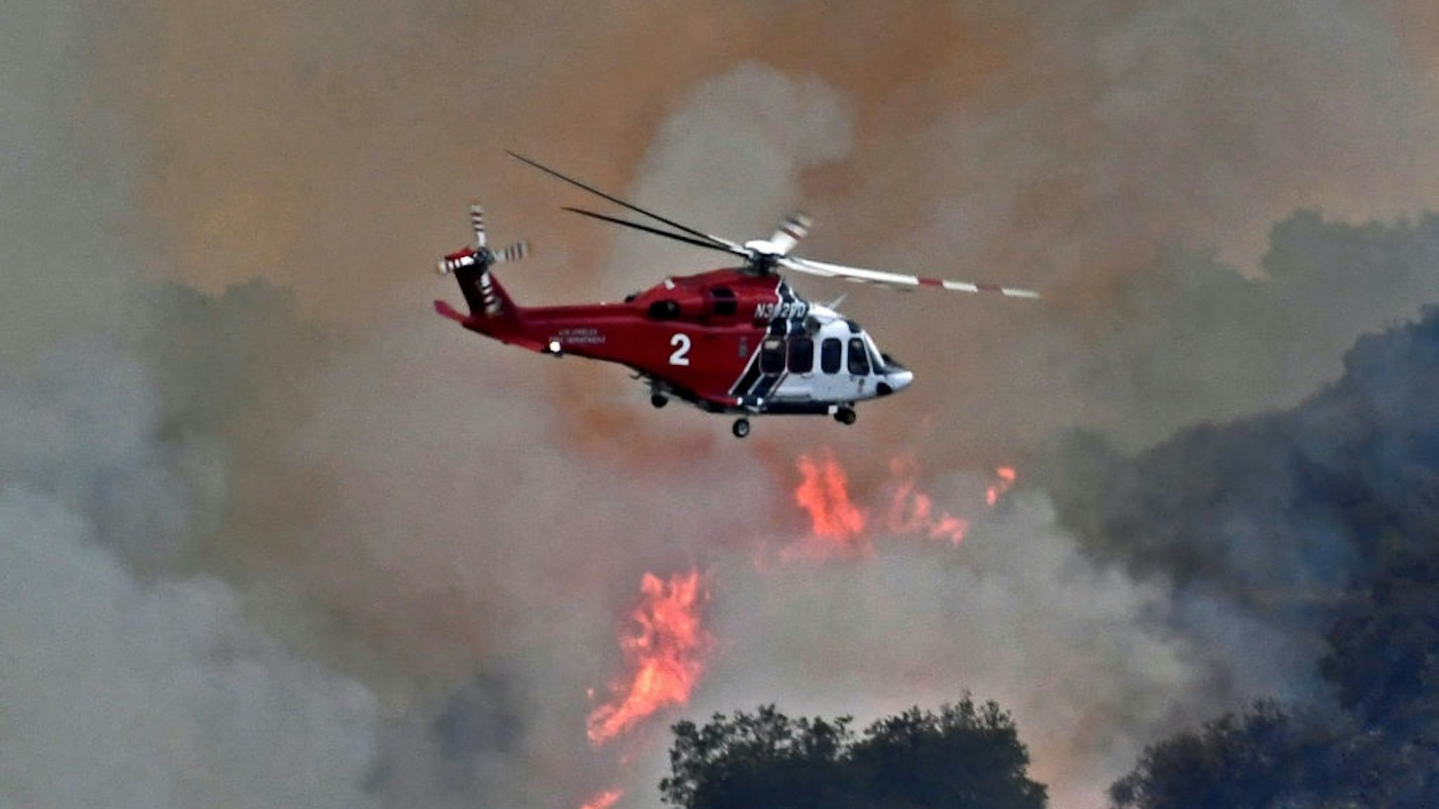 PACIFIC PALISADES, CA - MAY 16: A helicopter flies over as firefighters continue to battle a 1,325-acre brush fire May 16, 2021 near Pacific Palisades, California.