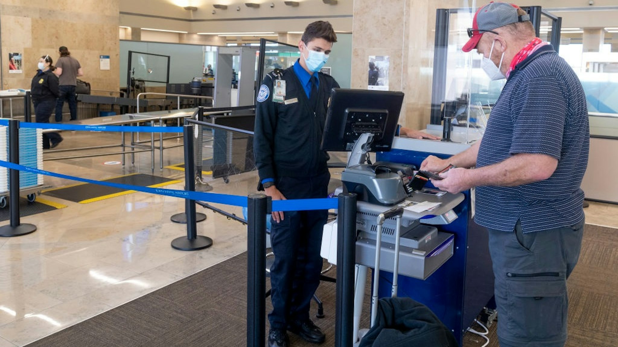 SANTA ANA, CA - JANUARY 26: A TSA agent helps a man through a security checkpoint at John Wayne Airport in Santa Ana, CA on Tuesday, January 26, 2021.