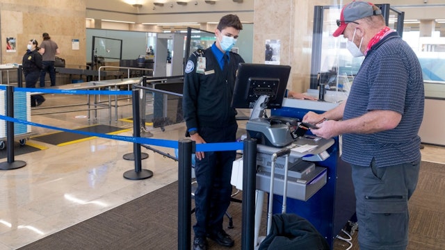 SANTA ANA, CA - JANUARY 26: A TSA agent helps a man through a security checkpoint at John Wayne Airport in Santa Ana, CA on Tuesday, January 26, 2021.
