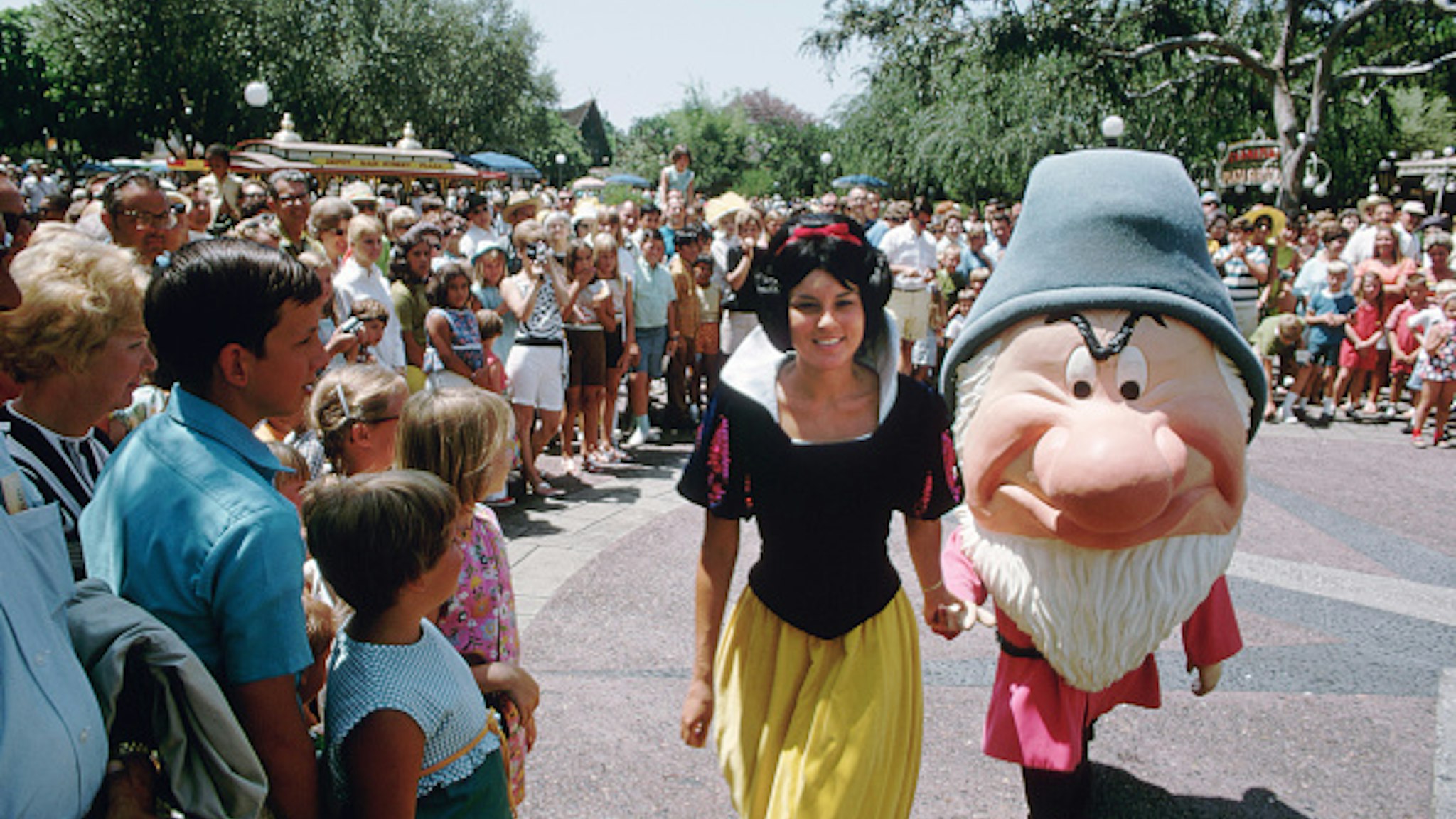 A crowd gathers to watch Snow White and Grumpy on a sunny day at Disneyland. Anaheim, California, 1969