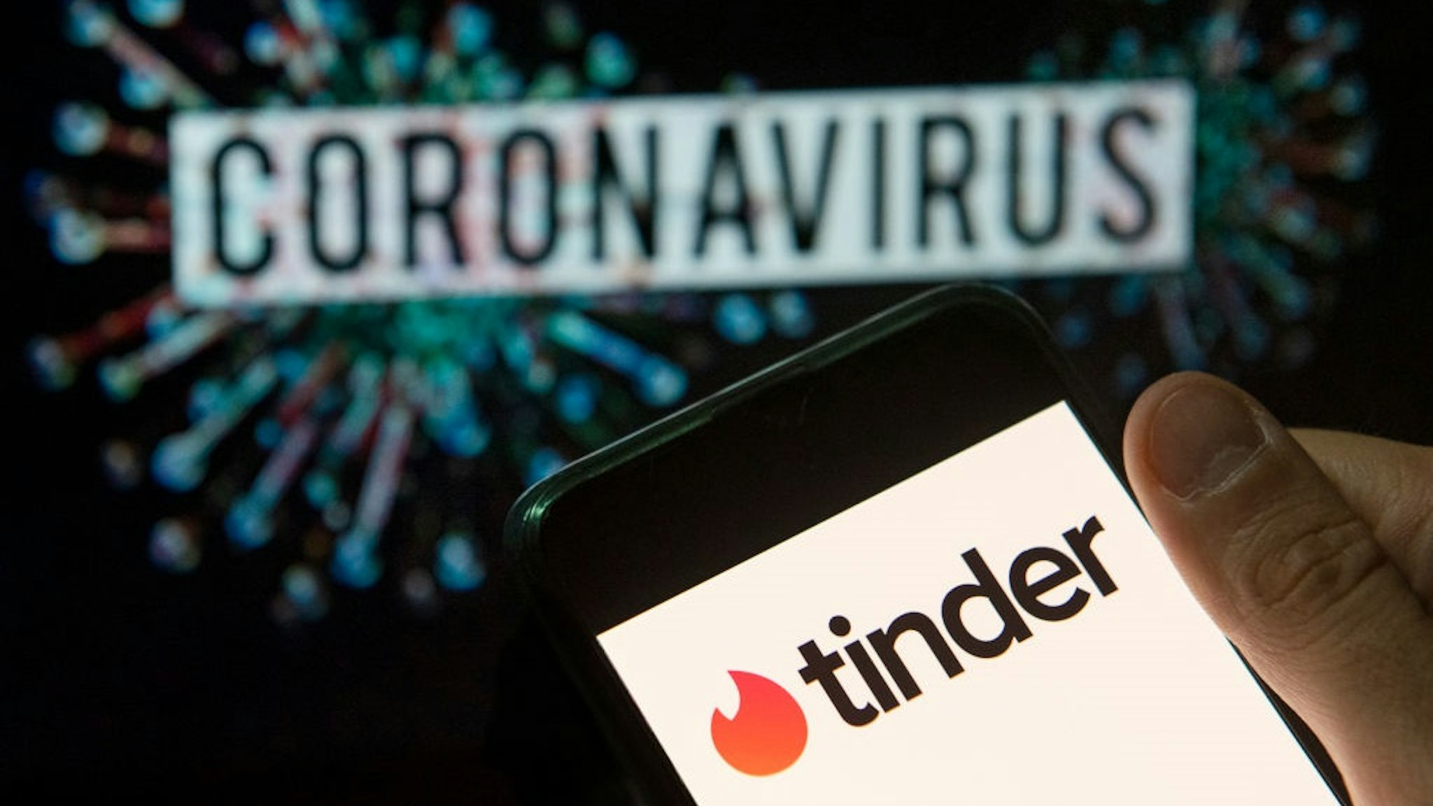 CHINA - 2020/03/22: In this photo illustration the mobile dating app Tinder logo seen displayed on a smartphone with a computer model of the COVID-19 coronavirus on the background.
