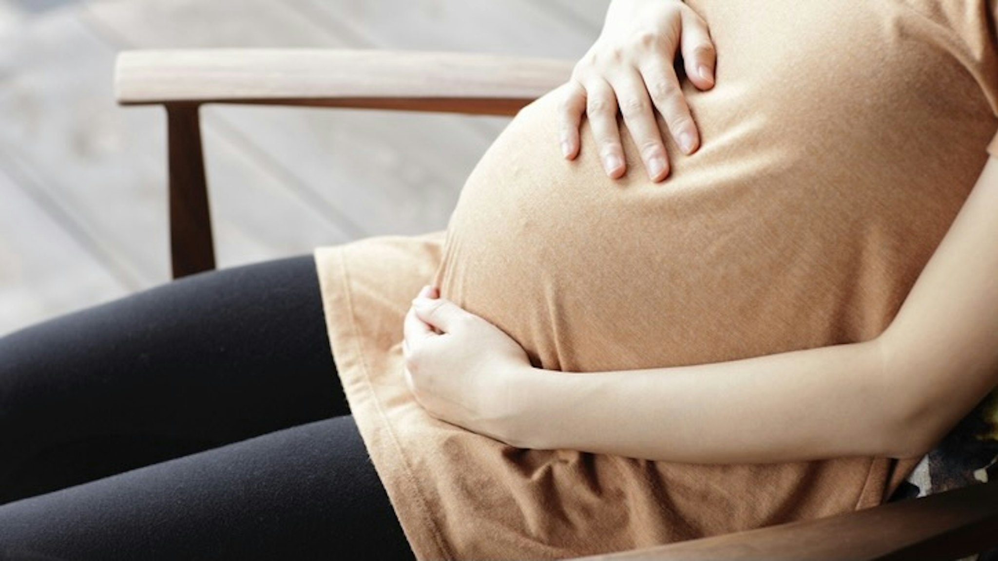 Pregnant woman touching abdomen sitting chair - stock photo sot via Getty Images