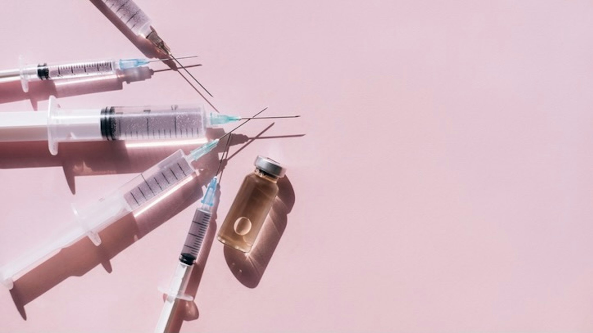 Bunch of syringes near vial of drug. Vaccination is the most anticipated procedure of the year. - stock photo Top view of set of clean syringes placed near glass bottle of medicine with air bubble on pink background. Vaccination is the most anticipated procedure of the year. Anna Efetova via Getty Images