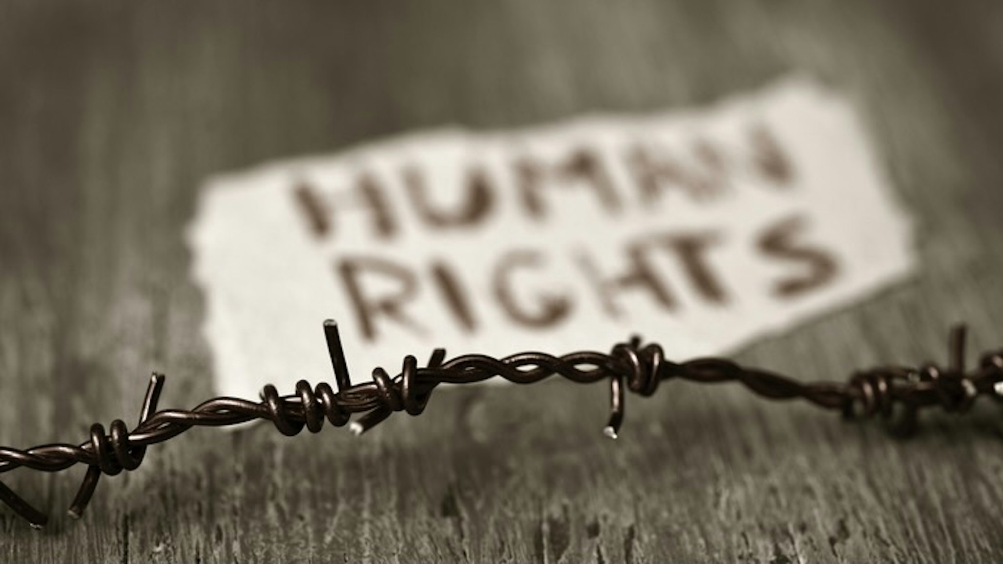 barbed wire and text human rights - stock photo closeup of a barbed wire and a piece of paper with the text human rights handwritten in it on a rustic wooden surface nito100 via Getty Images
