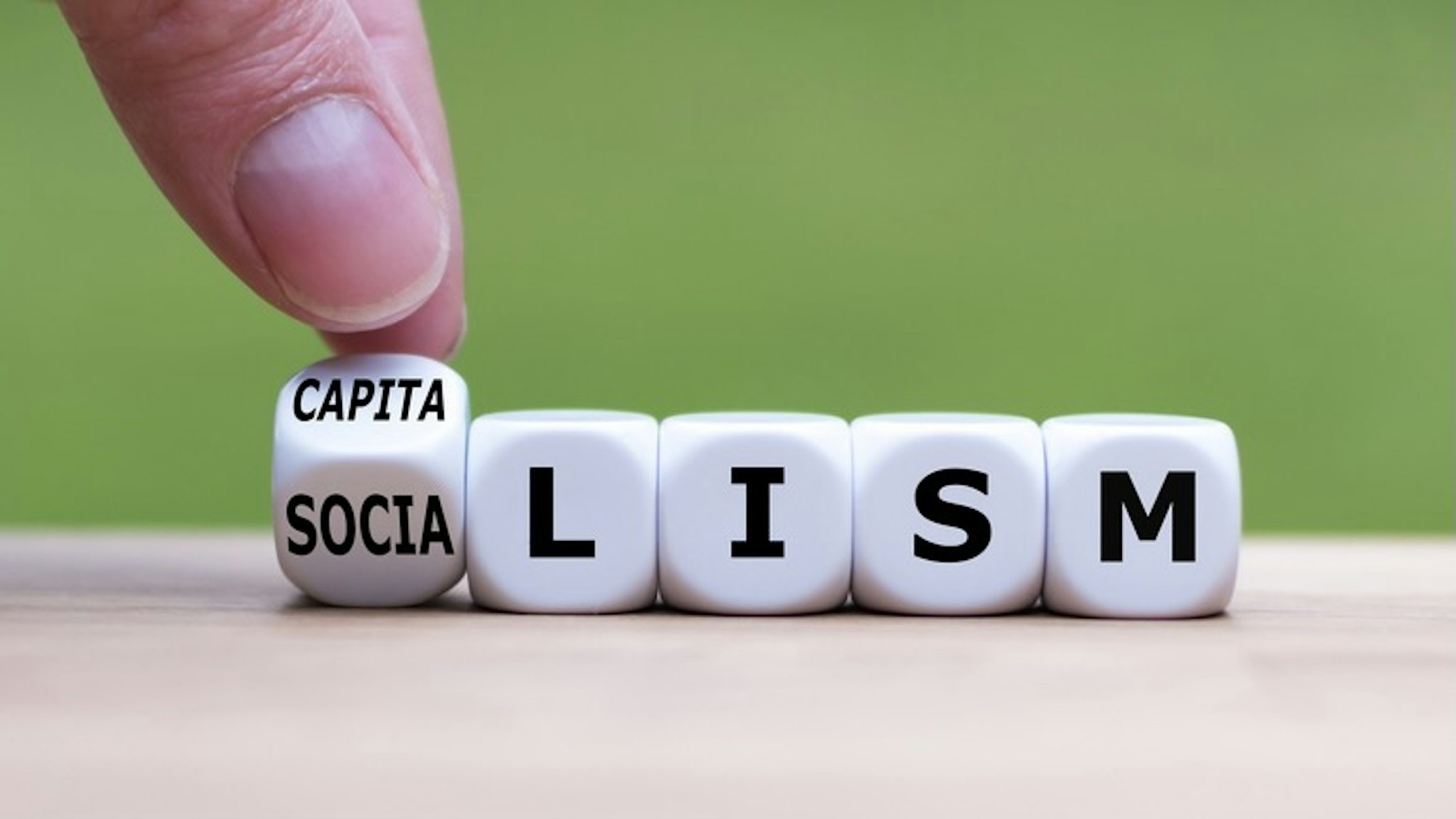 Hand flips a dice and changes the word "Socialism" to "Capitalism", or vice versa. - stock photo Hand flips a dice and changes the word "Socialism" to "Capitalism", or vice versa. Fokusiert via Getty Images