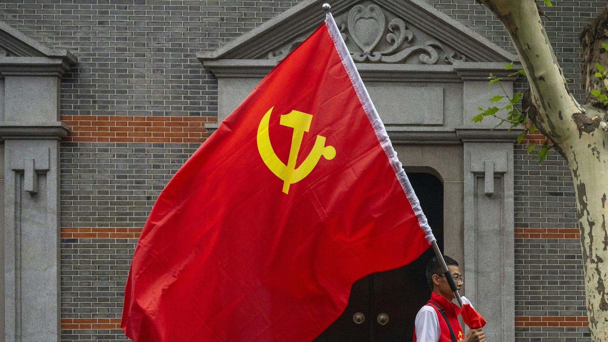 SHANGHAI, CHINA - JUNE 17: A man carries the hammer and sickle flag outside of the Memorial of the First National Congress of the Communist Party of China, on June 17, 2021 in Shanghai, China. The memorial, built where the first congress of the party was started before being interrupted by authorities in 1921, is considered, together with Nanhu Red Boat in Jiaxing, the physical birthplace of the CPC and it is one of the key sites of the so called "Red Tourism".