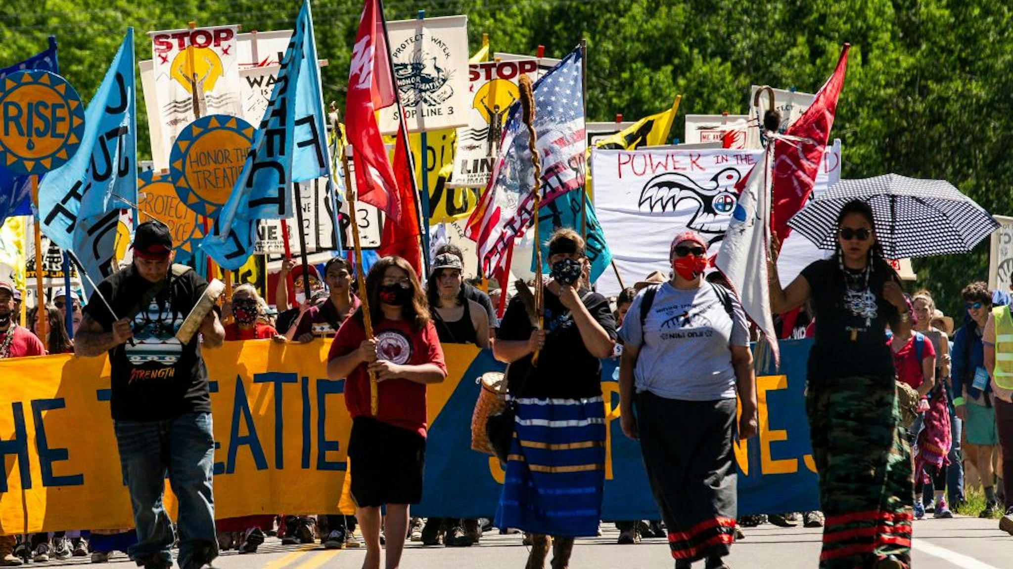 Climate activist and Indigenous community members hold a banner and flags during a rally and march in Solway, Minnesota on June 7, 2021. - Line 3 is an oil sands pipeline which runs from Hardisty, Alberta, Canada to Superior, Wisconsin in the United States. In 2014, a new route for the Line 3 pipeline was proposed to allow an increased volume of oil to be transported daily. While that project has been approved in Canada, Wisconsin, and North Dakota, it has sparked continued resistance from climate justice groups and Native American communities in Minnesota. While many people are concerned about potential oil spills along Line 3, some Native American communities in Minnesota have opposed the project on the basis of treaty rights and calling President Biden to revoke the permits and halt construction. (Photo by Kerem Yucel / AFP) (Photo by KEREM YUCEL/AFP via Getty Images)