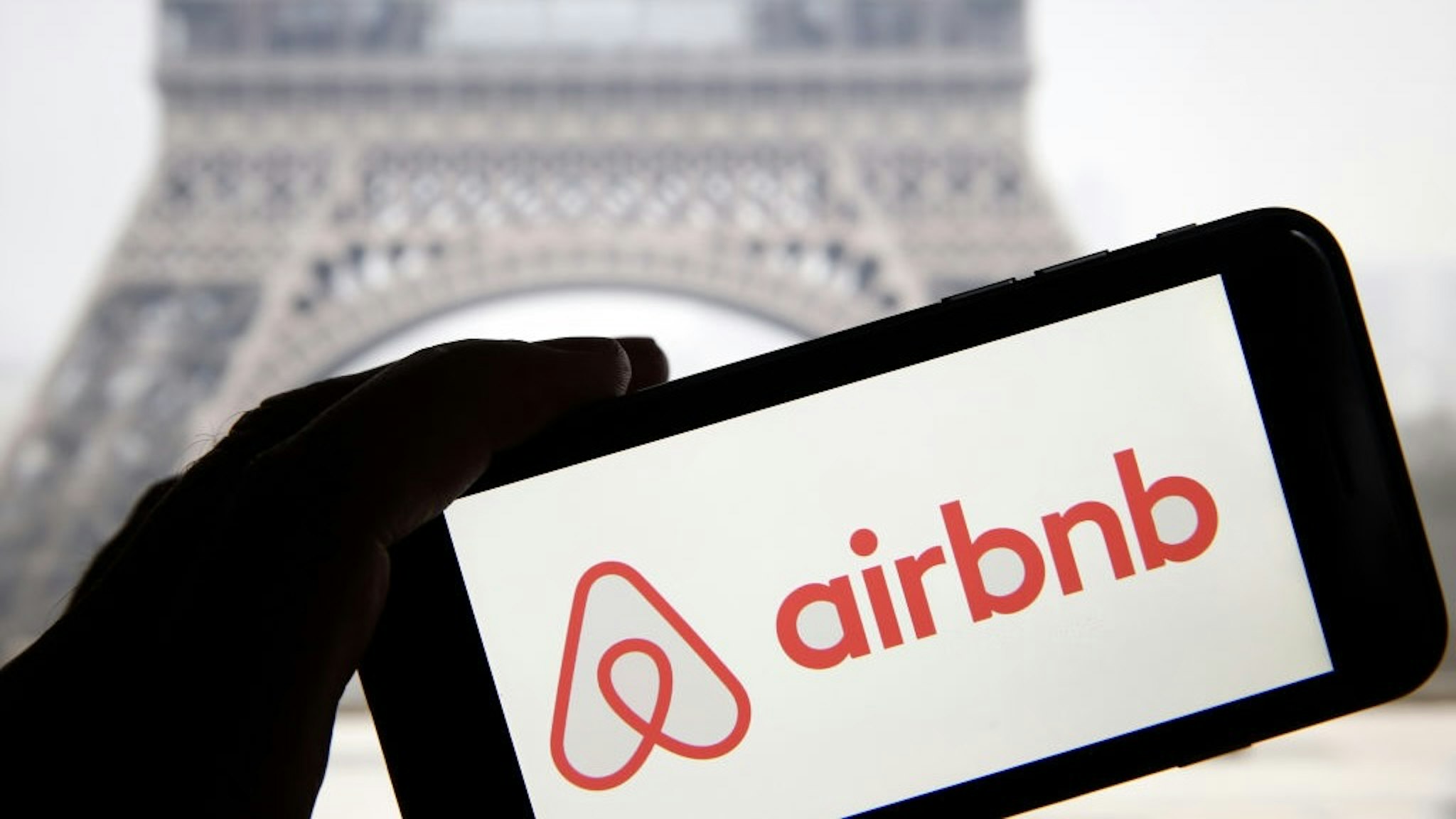 Airbnb : Illustration PARIS, FRANCE - FEBRUARY 11: In this photo illustration, the Airbnb logo is displayed on the screen of an iPhone in front of a computer screen displaying a picture of the Eiffel Tower on February 11, 2019 in Paris, France. Paris is one of the most popular destinations for Airbnb, but city authorities do not agree with the private rental and booking company. The mayor of Paris, Anne Hidalgo, announced Sunday that the city would sue Airbnb for 14 million dollars, because of the alleged list of 1,000 illegal rentals. (Photo by Chesnot/Getty Images) Chesnot / Contributor via Getty Images