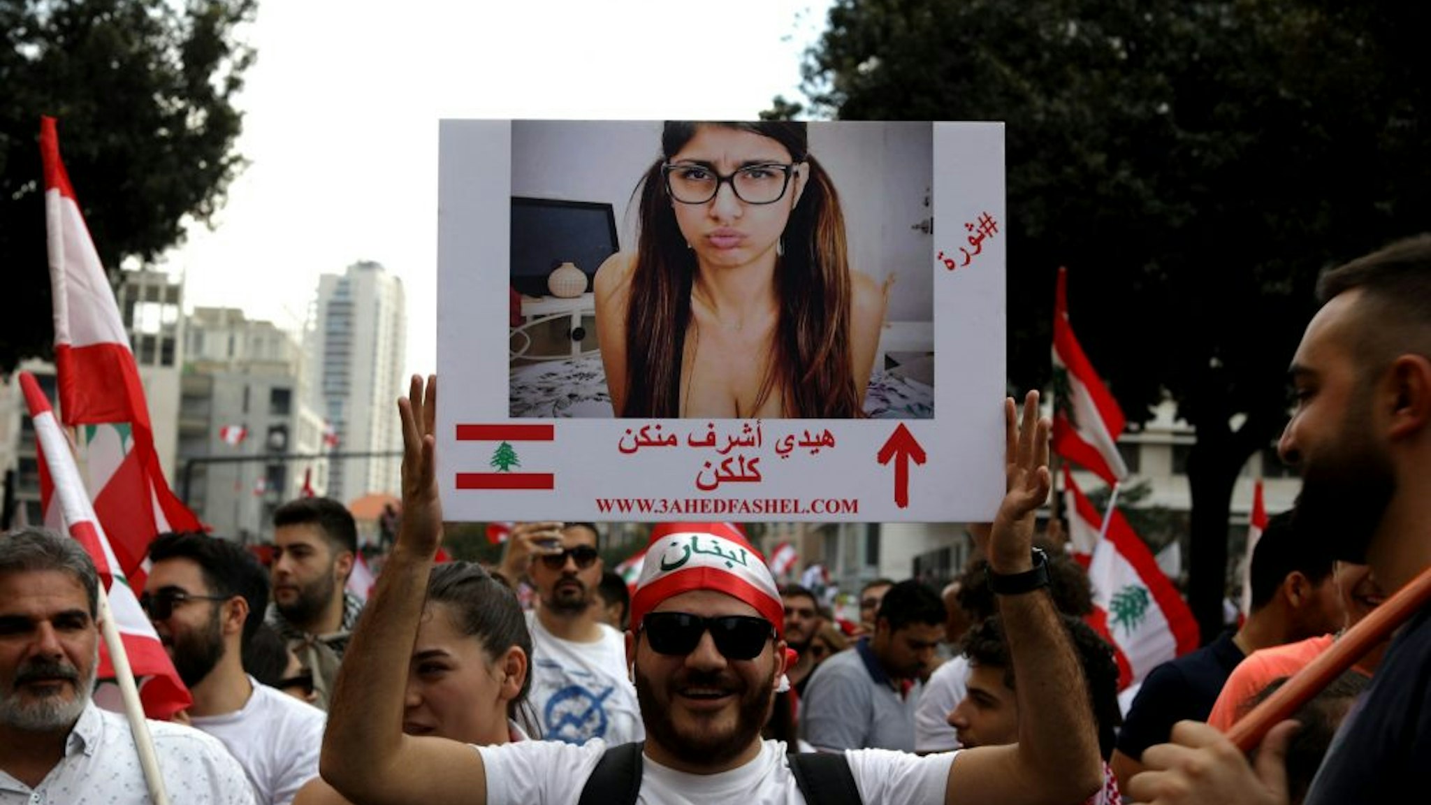 A Lebanese man holds a picture of Lebanese porn actress Mia Khalifa as he takes part in a rally in downtown Beirut on October 20, 2019, on the fourth day of demonstrations against tax increases and official corruption. The writing on the placard reads in Arabic " She is more honourable than all of you". - Thousands continued to rally despite calls for calm from politicians and dozens of arrests. The demonstrators are demanding a sweeping overhaul of Lebanon's political system, citing grievances ranging from austerity measures to poor infrastructure.