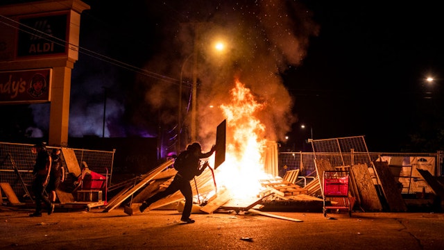 A protester throws a piece of wood on a fire in the street just north of the 3rd Police Precinct on May 27, 2020 in Minneapolis, Minnesota.