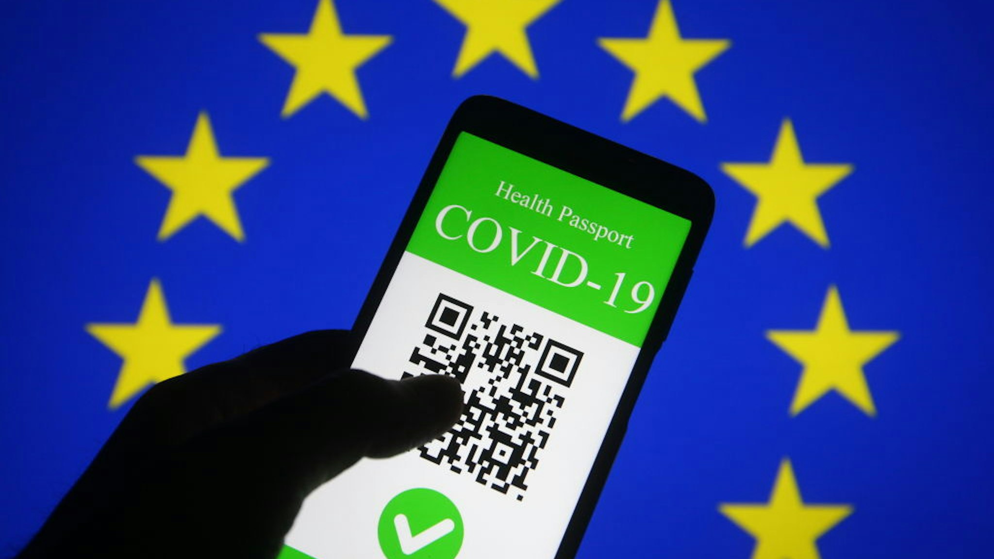 UKRAINE - 2021/03/28: In this photo illustration, a symbolic COVID-19 health passport seen displayed on a smartphone screen in front of the EU flag. On March 17 the European Commission presented a proposal to create a Digital Green Certificate to facilitate the safe free movement of the EU citizens during the COVID-19 pandemic.