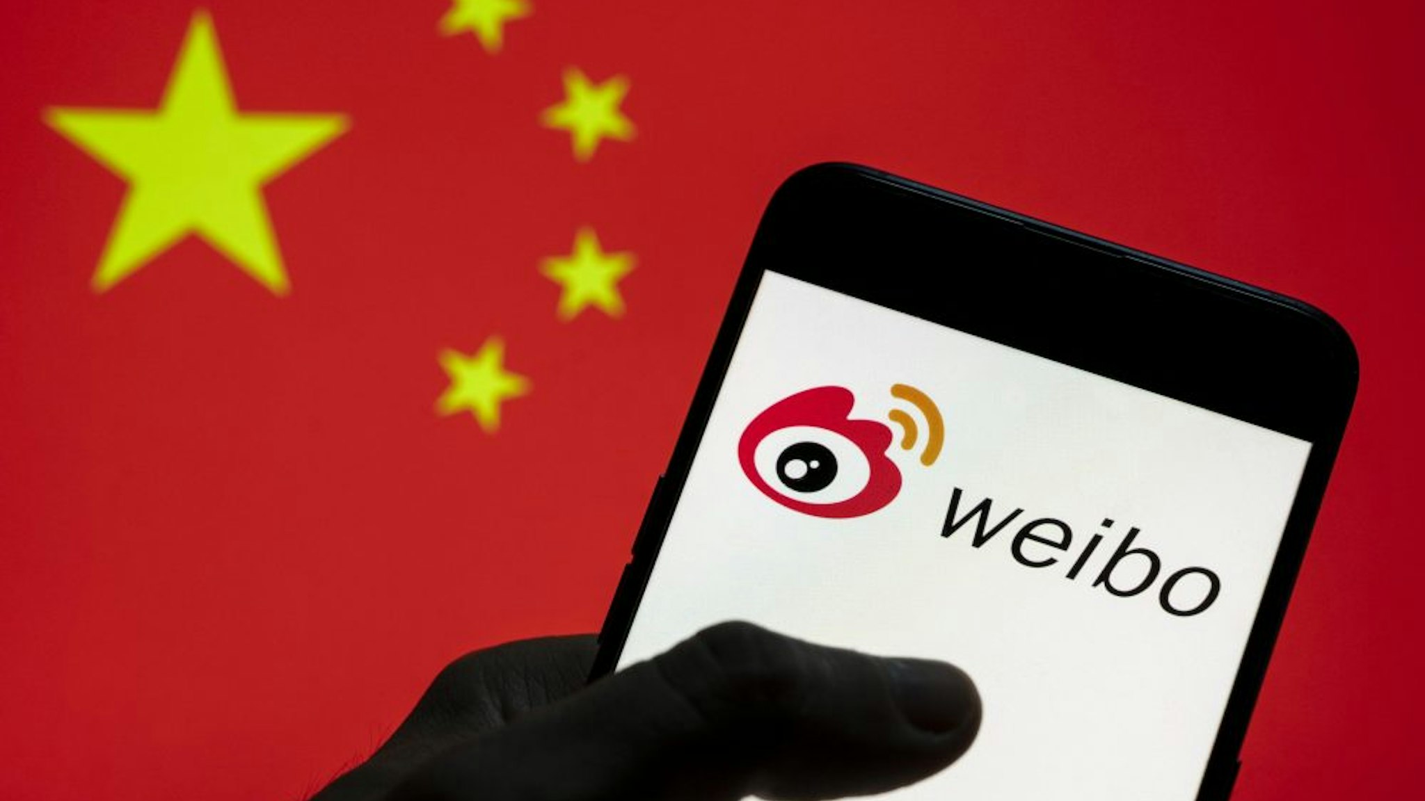 CHINA - 2021/03/28: In this photo illustration the Chinese social media platform Weibo logo seen on an Android mobile device with People's Republic of China flag in the background.