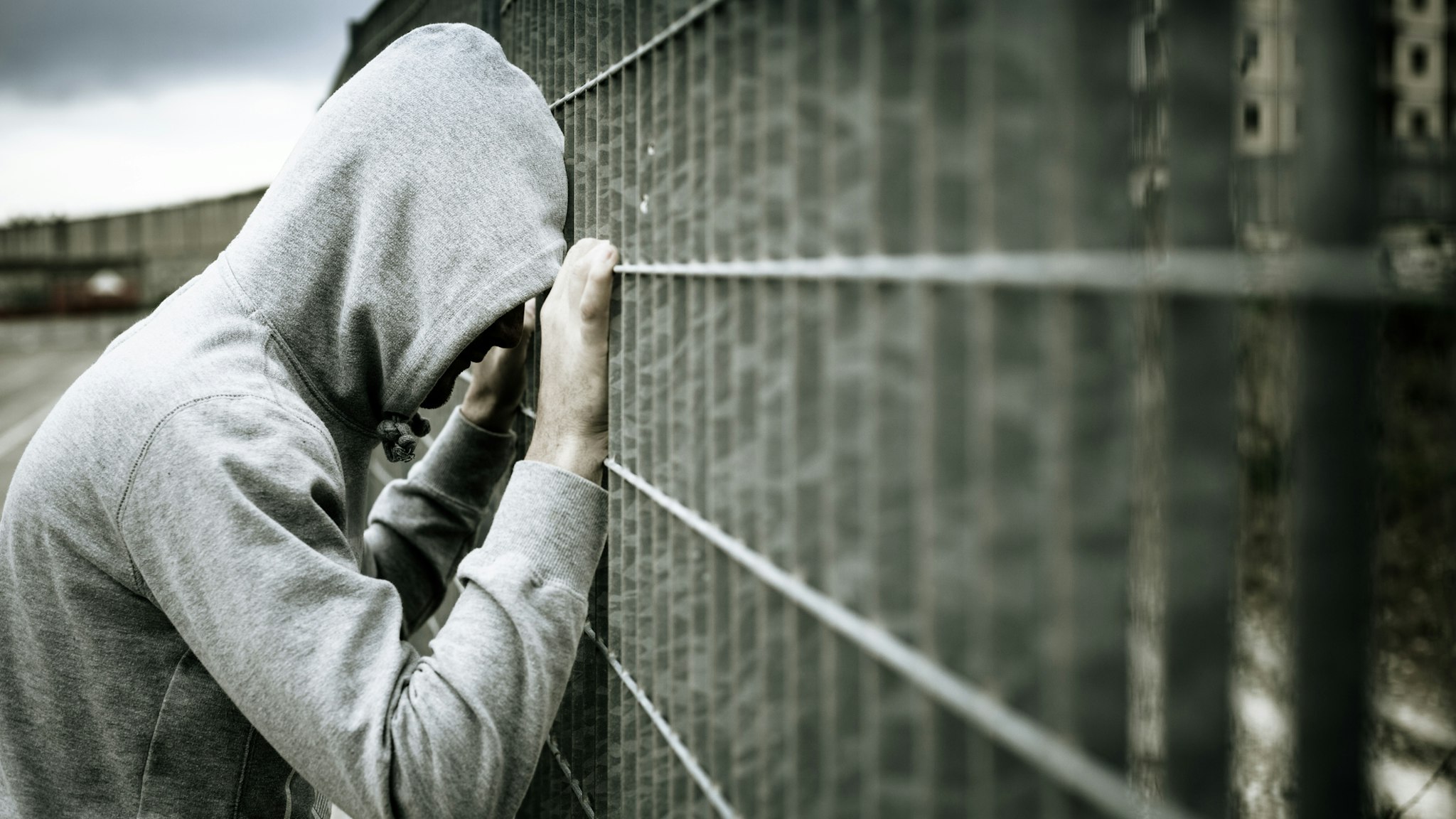 Lonely Man with Hood Leaning on a Fence - stock photo