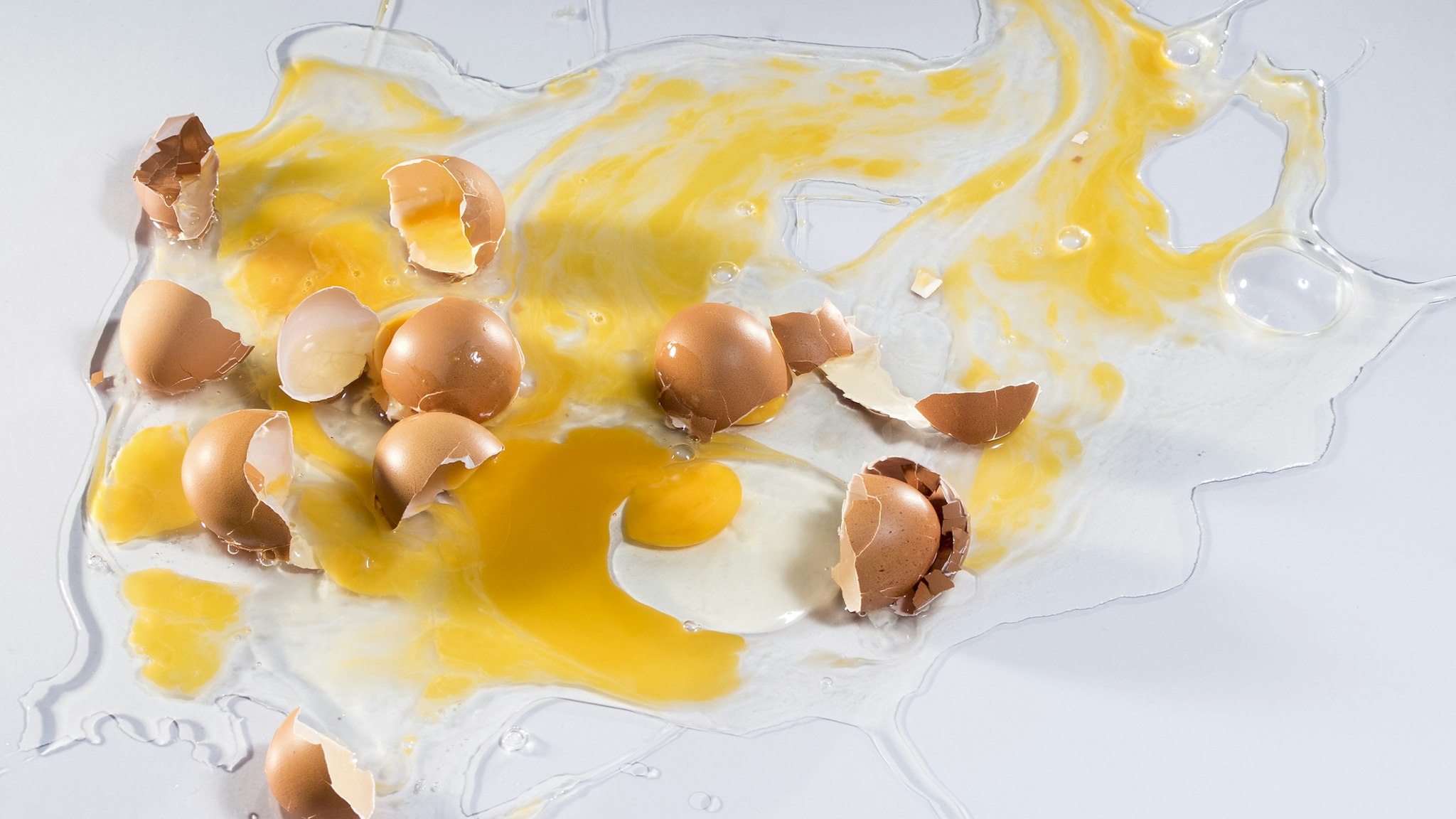 Complete setting of eggs broken by impacts on a white surface - stock photo