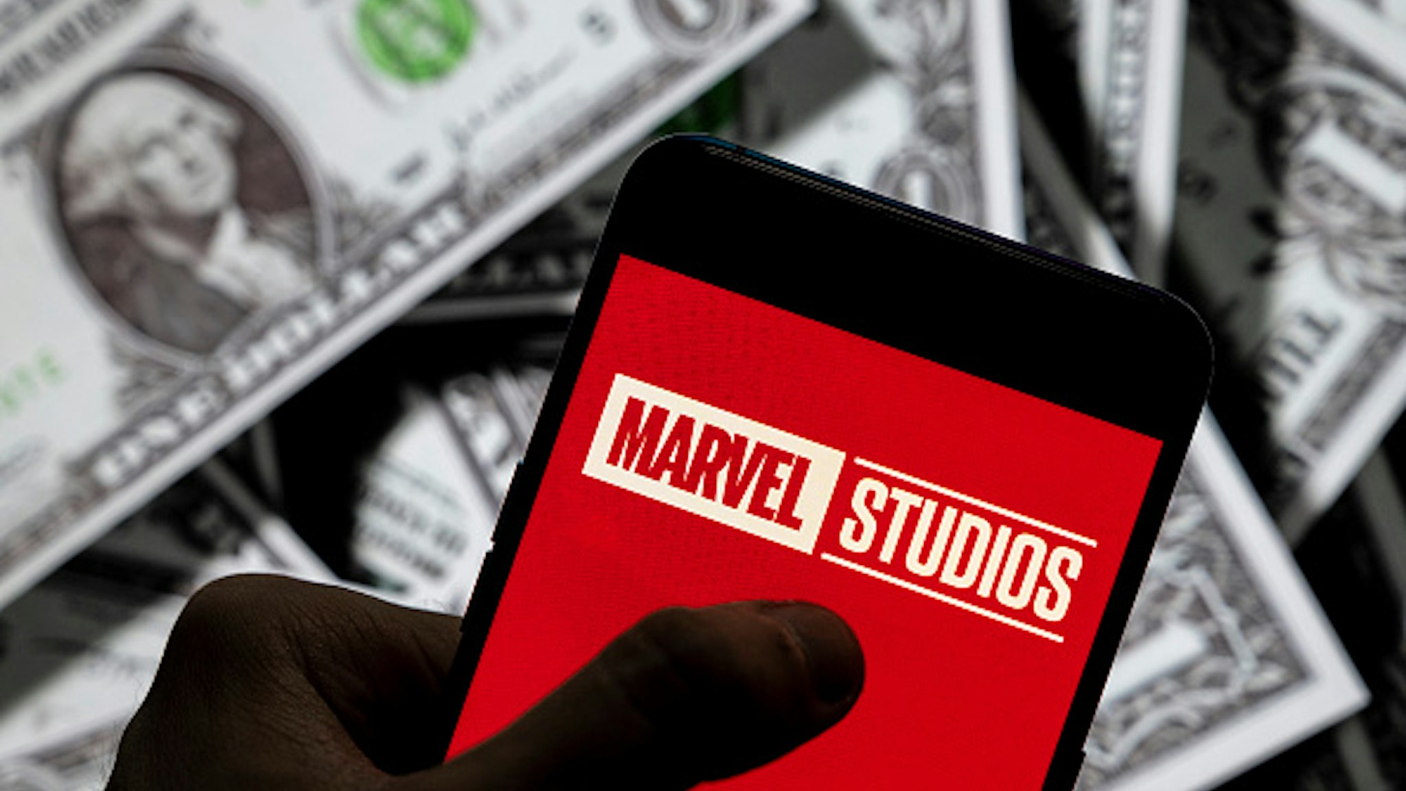 CHINA - 2021/04/23: In this photo illustration, a Marvel Studios logo seen displayed on a smartphone with USD (United States dollar) currency in the background.