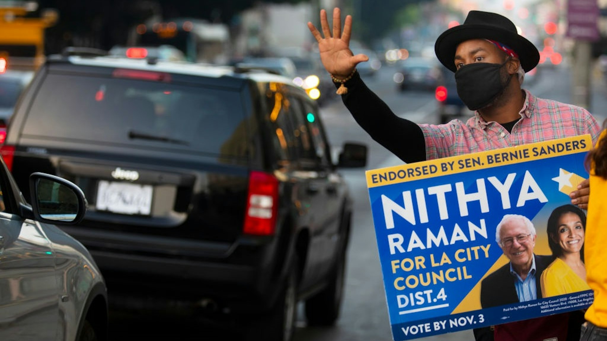 LOS ANGELES, CA - NOVEMBER 03: As the sun begins to set Matthew Gaston, 37, of Los Angeles, holds up a vote sign for Nithya Raman for LA City Council down the street from a voting center inside The Wiltern on election day on Tuesday, Nov. 3, 2020 in Los Angeles, CA.