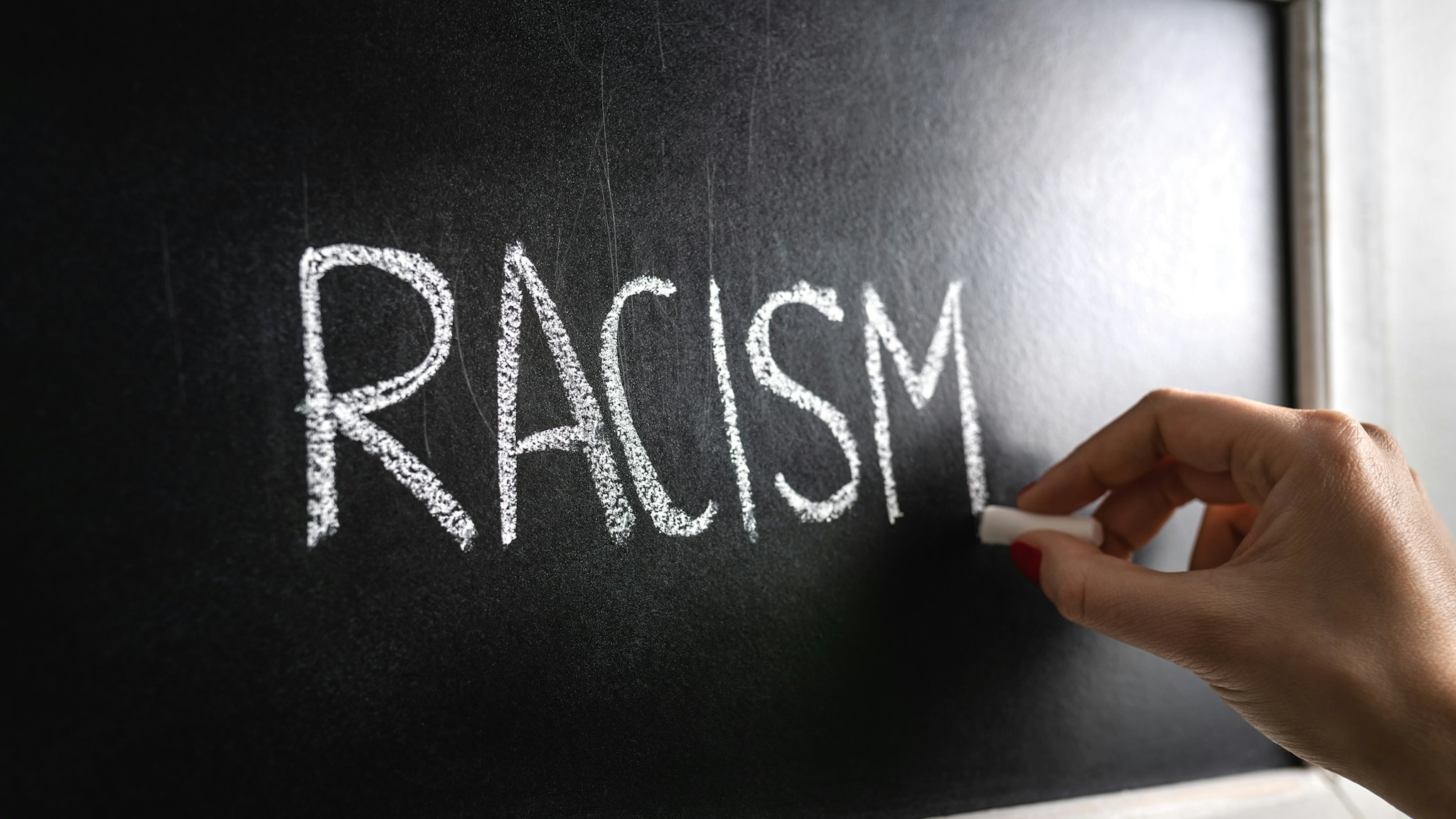 Hand writing the word racism on blackboard.