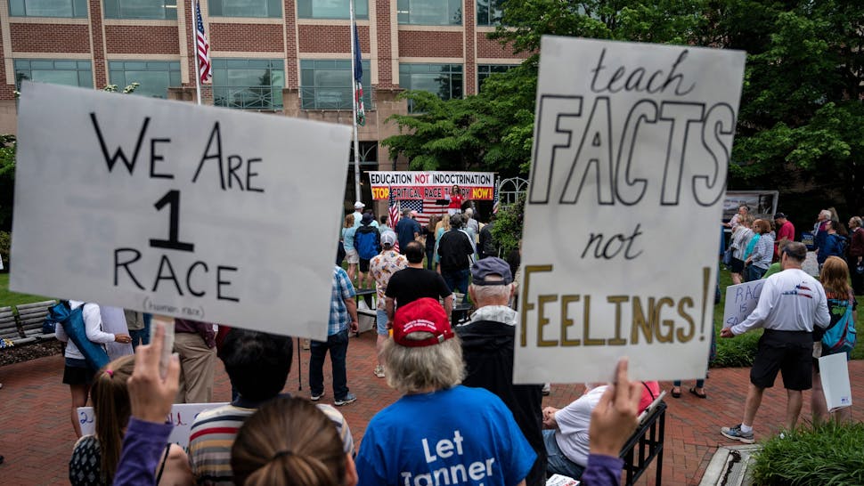 Teach Facts Not Feelings People hold up signs during a rally against "critical race theory" (CRT) being taught in schools at the Loudoun County Government center in Leesburg, Virginia on June 12, 2021. - "Are you ready to take back our schools?" Republican activist Patti Menders shouted at a rally opposing anti-racism teaching that critics like her say trains white children to see themselves as "oppressors." "Yes!", answered in unison the hundreds of demonstrators gathered this weekend near Washington to fight against "critical race theory," the latest battleground of America's ongoing culture wars. The term "critical race theory" defines a strand of thought that appeared in American law schools in the late 1970s and which looks at racism as a system, enabled by laws and institutions, rather than at the level of individual prejudices. But critics use it as a catch-all phrase that attacks teachers' efforts to confront dark episodes in American history, including slavery and segregation, as well as to tackle racist stereotypes. (Photo by ANDREW CABALLERO-REYNOLDS / AFP)