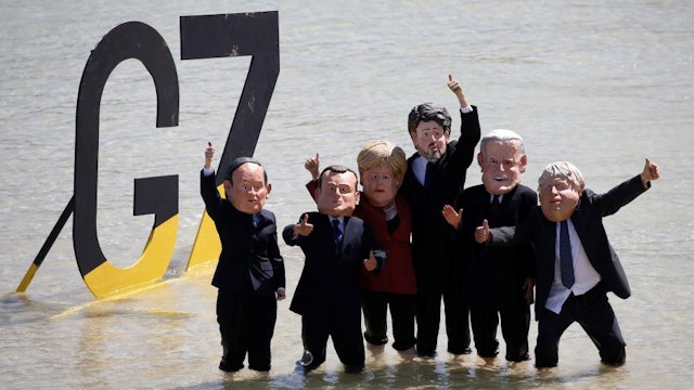 Extinction Rebellion protesters stand in front of a G7 sign wearing masks depicting from left to right, Yoshihide Suga, Japan's prime minister, Emmanuel Macron, France's president, Angela Merkel, Germany's chancellor, Justin Trudeau, Canada's prime minister, U.S. President Joe Biden, and Boris Johnson, U.K. prime minister, on the beach on the sidelines of the final day of the Group of Seven leaders summit, in St. Ives, U.K., on Sunday, June 13, 2021. The worlds richest governments are under mounting pressure to help poor countries fight climate change. Photographer: