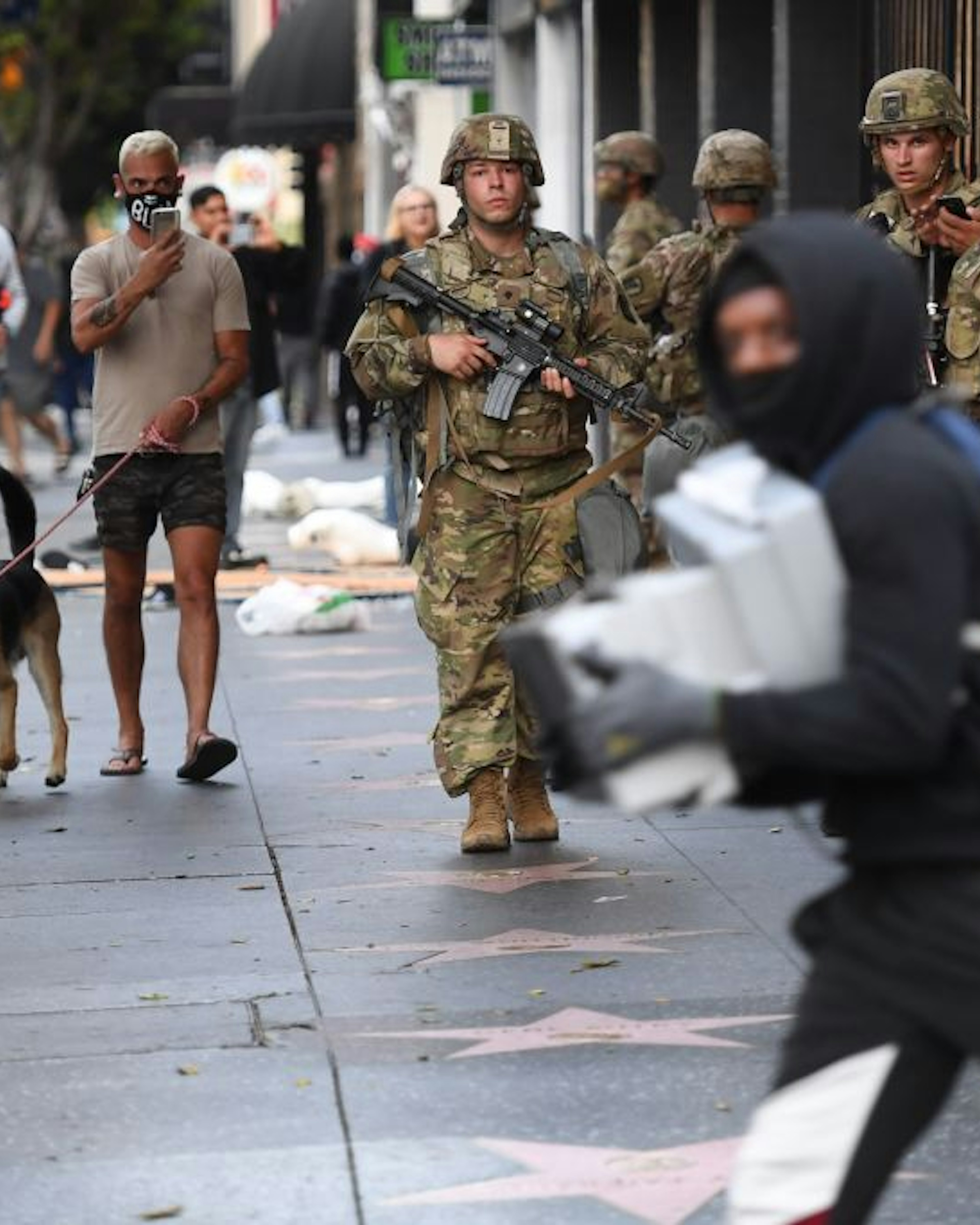TOPSHOT - A suspected looter carrying boxes of shoes run past National Guard soldiers in Hollywood, California, June 1, 2020, after a demonstration over the death of George Floyd. - Major US cities -- convulsed by protests, clashes with police and looting since the death in Minneapolis police custody of George Floyd a week ago -- braced Monday for another night of unrest. More than 40 cities have imposed curfews after consecutive nights of tension that included looting and the trashing of parked cars. (Photo by Robyn Beck / AFP) (Photo by ROBYN BECK/AFP via Getty Images)