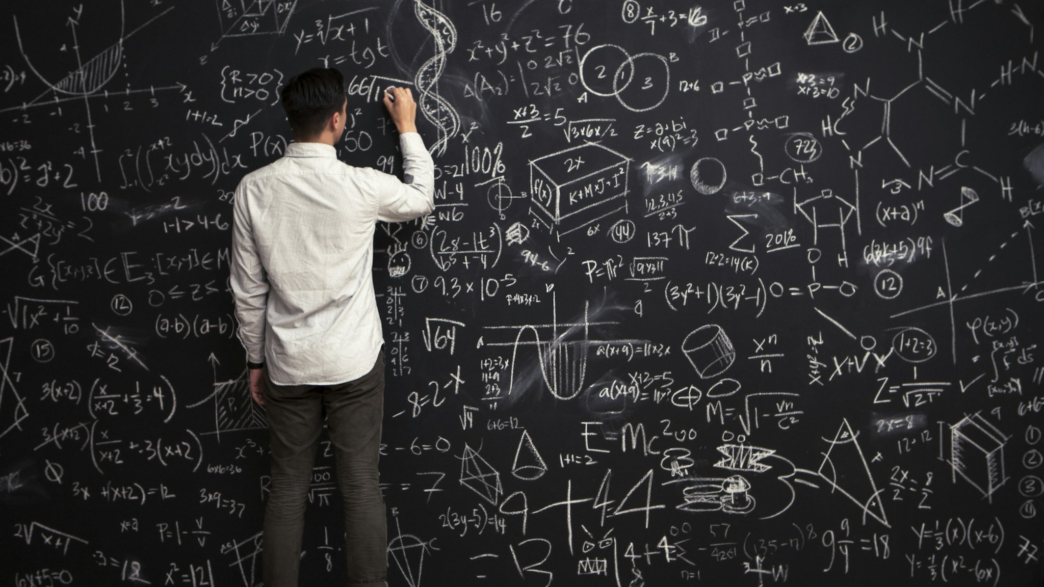 Man writes mathematical equations on chalkboard - stock photo