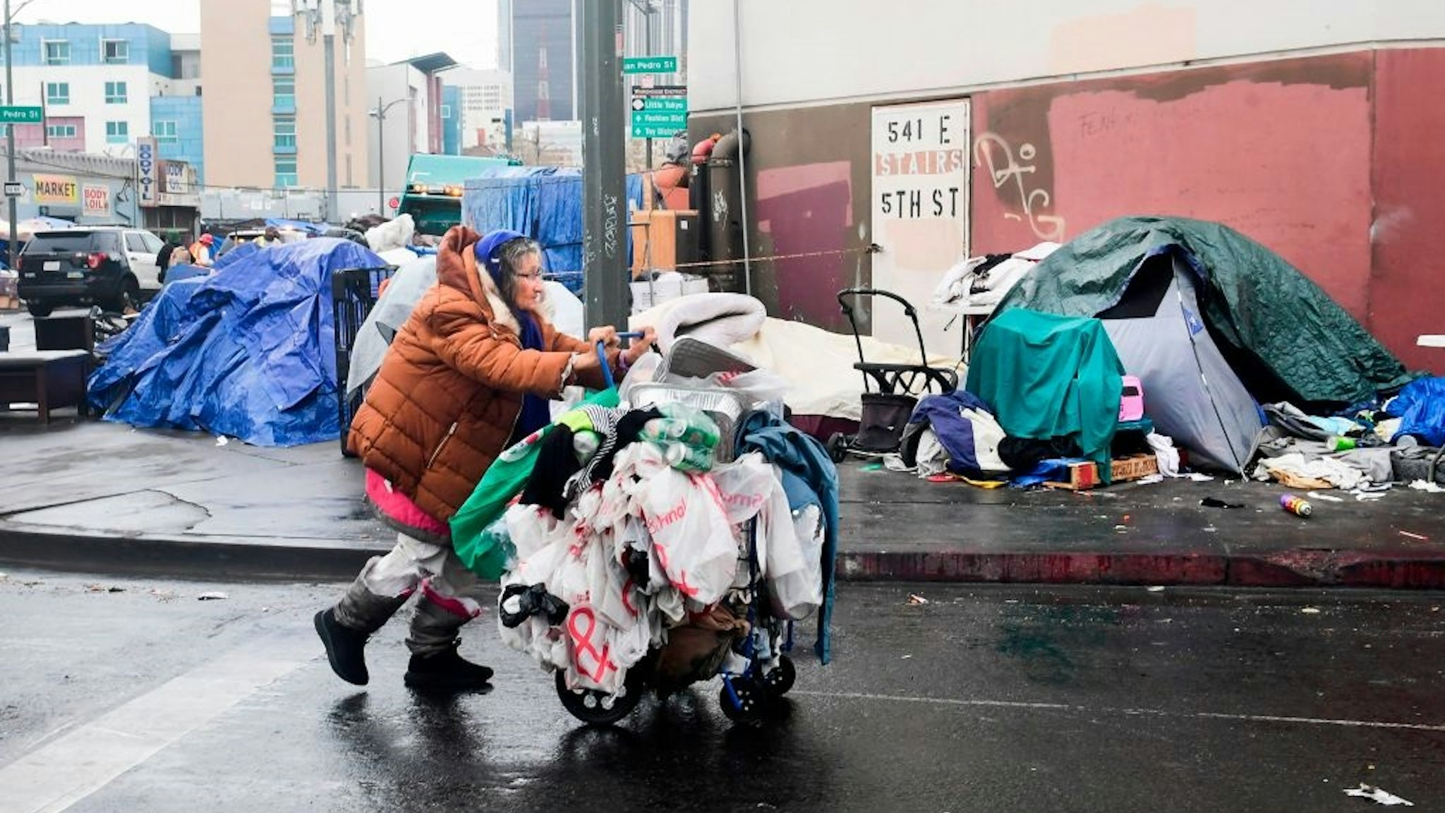 A homeless woman pushes her belongings past a row of tents on the streets of Los Angeles, California on February 1, 2021.