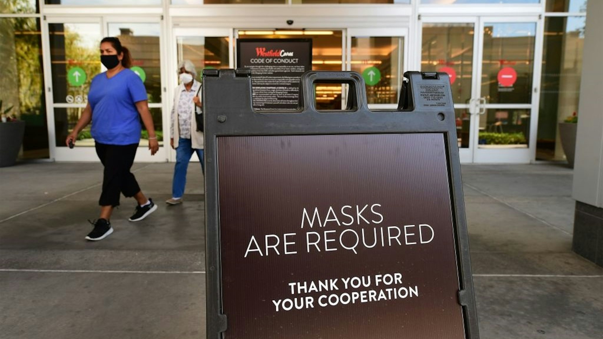 Women wearing facemasks exit a shopping mall where a sign is posted at an entrance reminding people of the mask requirement Westfield Santa Anita shopping mall on June 12, 2020 in Arcadia, California.
