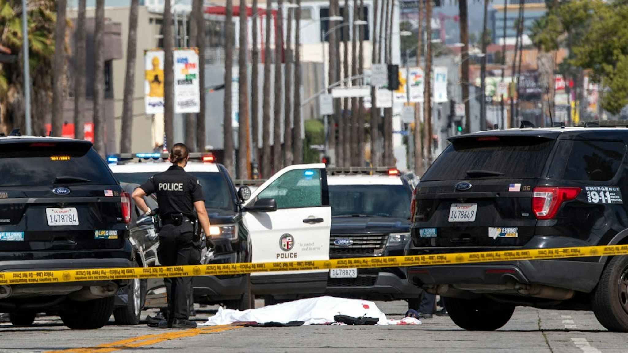 A LAPD police officer stands at the corner of Fairfax Avenue and Sunset Boulevard where a body covered in a white sheet lies on the pavement in Los Angeles on April 24, 2021 in what appears to be an officer-involved shooting.
