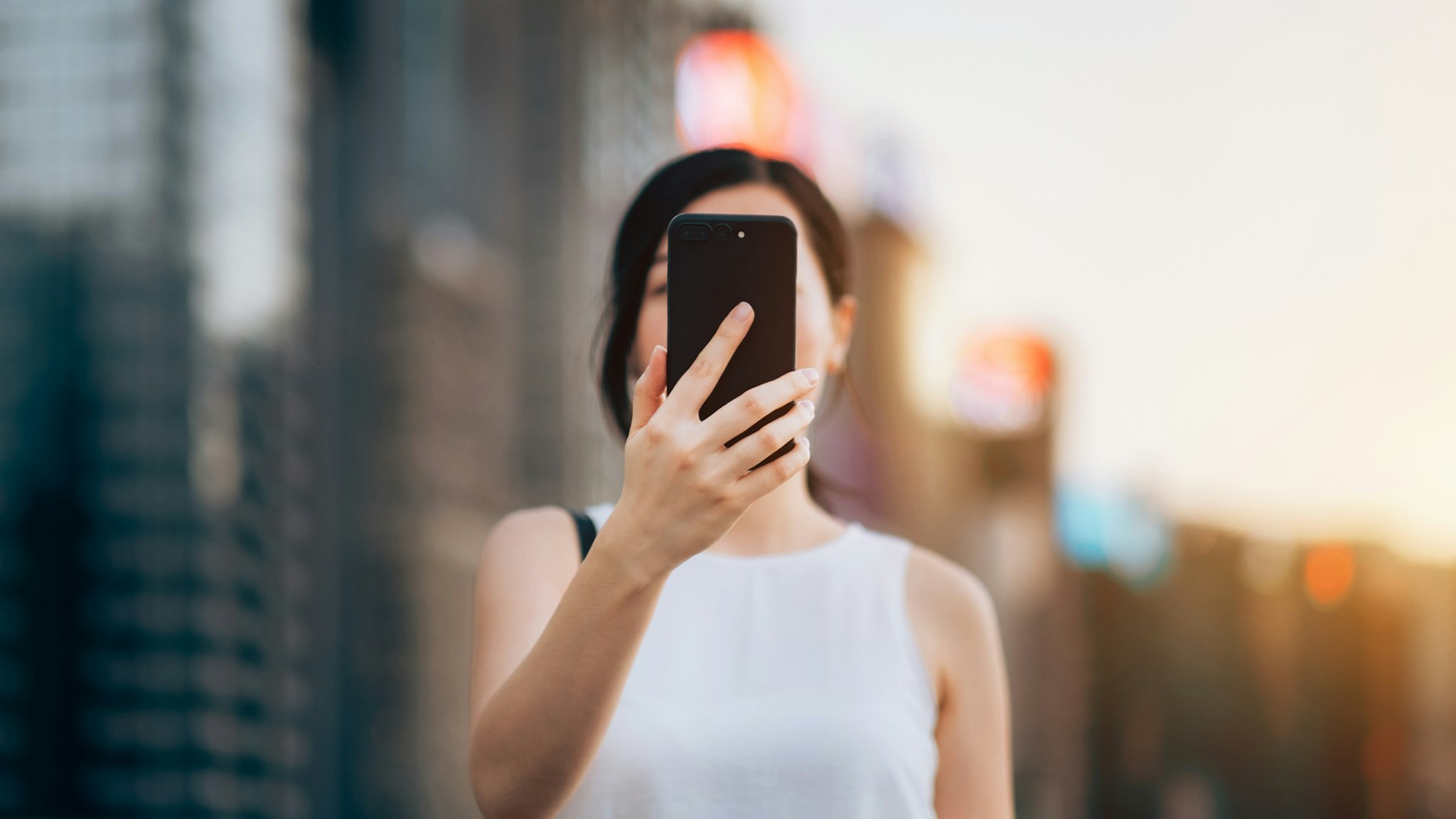 Young woman using smartphone outdoors in front of blurry city scene