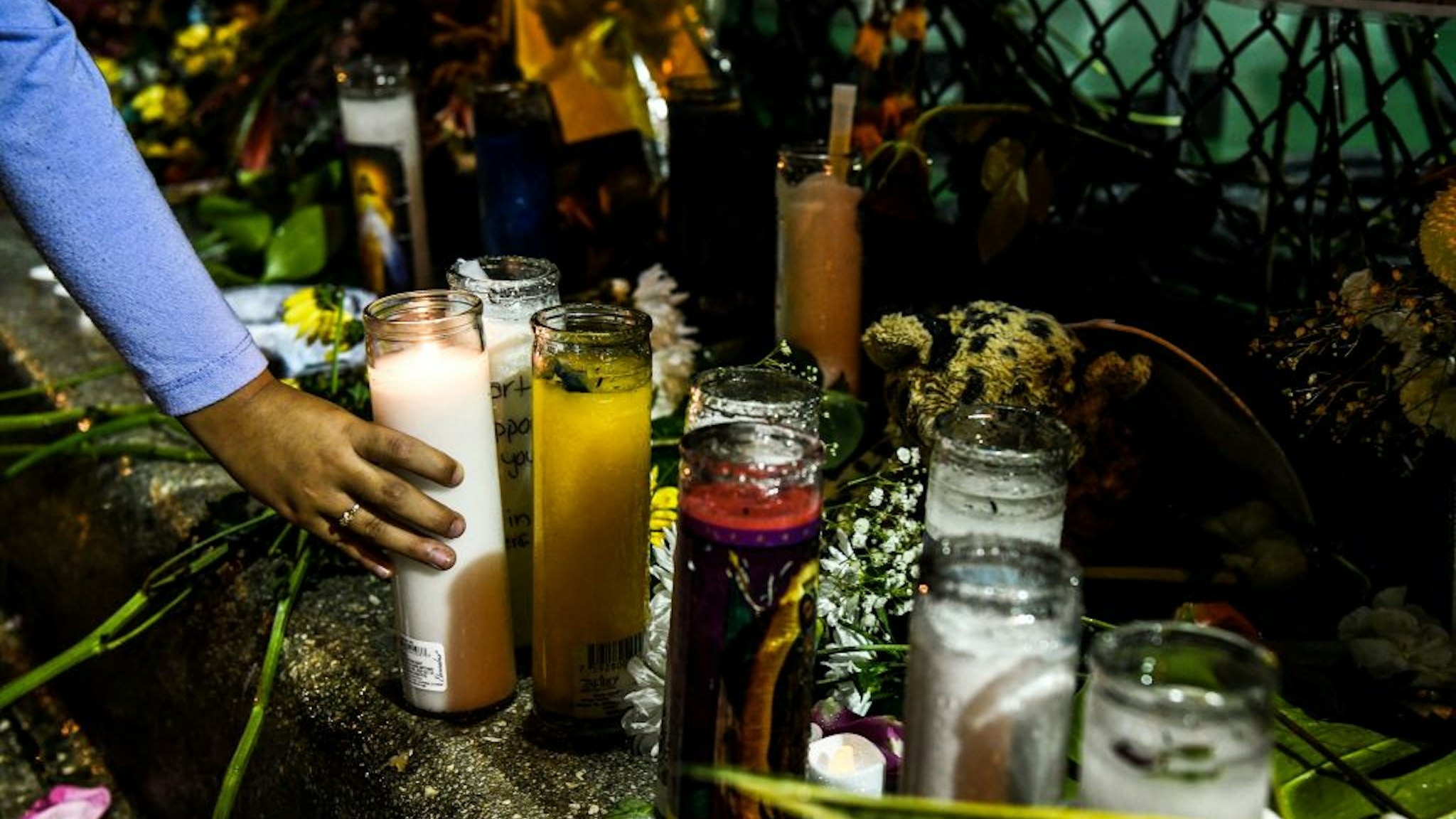 Salome Piedrahita lights a candle at the makeshift memorial for the victims of the building collapse, near the site of the accident in Surfside, Florida, north of Miami Beach on June 30, 2021. - Four more bodies were discovered overnight in the rubble of a collapsed apartment building in Florida, authorities said Wednesday, as the search for more than 140 people unaccounted for entered its seventh day. The official death toll now stands at 16 after most of a building in the Miami-area town of Surfside suddenly pancaked early last Thursday, but hopes are dwindling that the hundreds of rescuers combing the oceanfront site will find anyone alive.