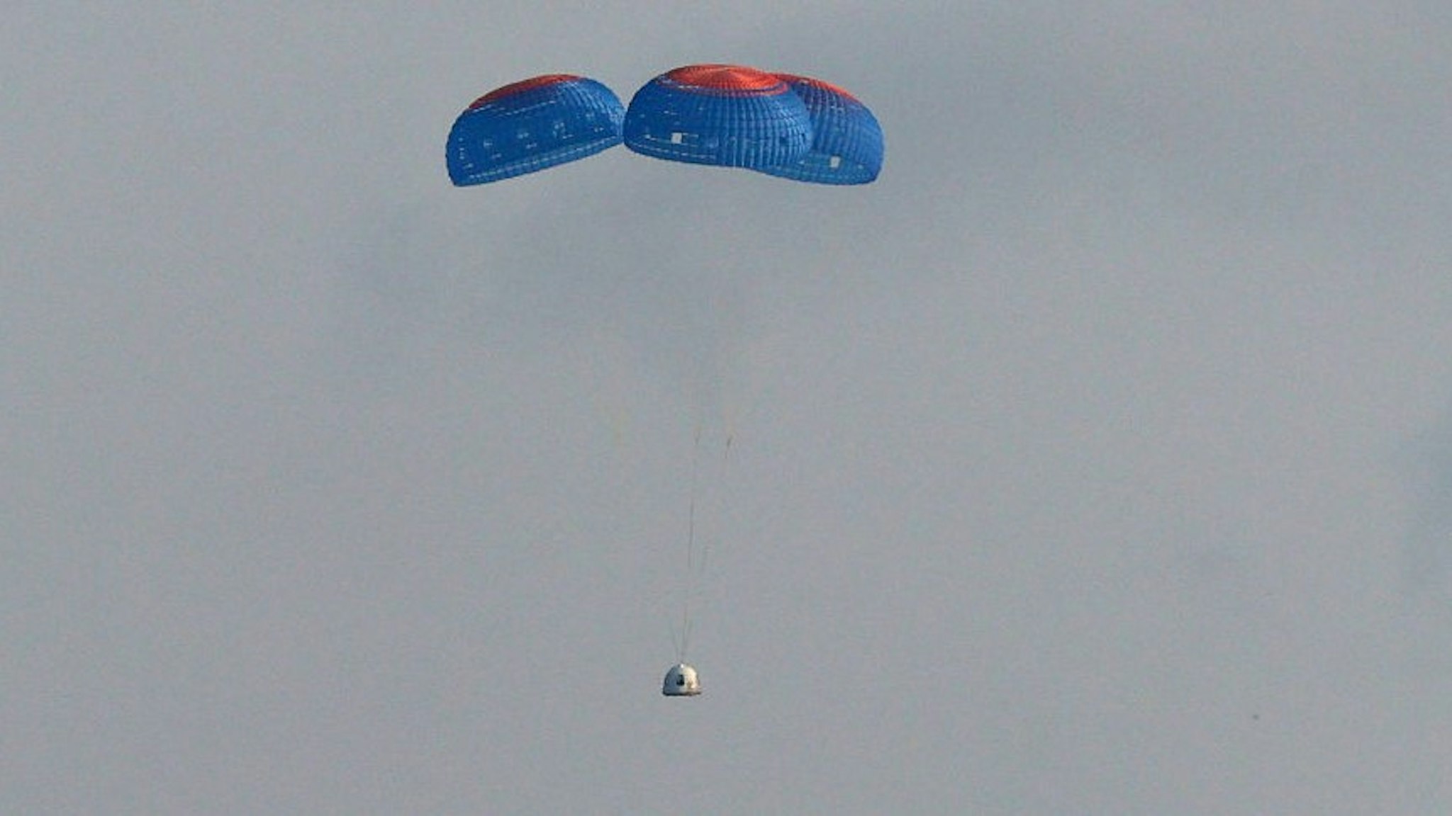 VAN HORN, TEXAS - JULY 20: Blue Origin’s New Shepard crew capsule descends on the end of its parachute system carrying Jeff Bezos along with his brother Mark Bezos, 18-year-old Oliver Daemen, and 82-year-old Wally Funk on July 20, 2021 in Van Horn, Texas. Mr. Bezos and the crew are riding in the first human spaceflight for the company. (Photo by