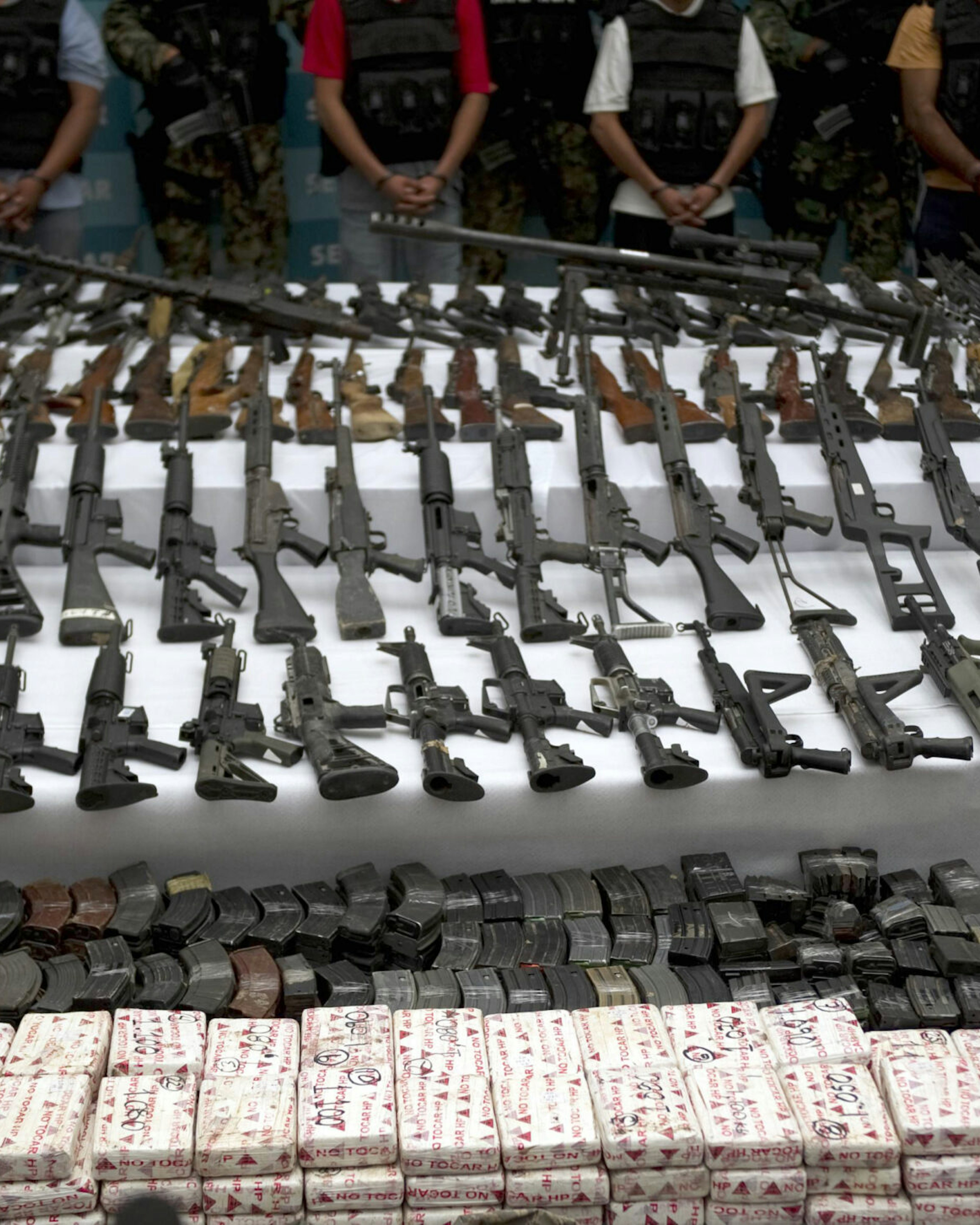 Mexican marines escort five alleged drug traffickers of the Zetas drug cartel in front of hand grenades, firearms, cocaine and military uniforms seized to alleged members of the Zetas drug traffickers cartel and presented to press on June 9, 2011 at the Navy Secretaryship in Mexico City. Fiven men were arrested and more than two hundred rifles, eleven pistols, military uniforms, differents caliber ammunitions and more than 200 kg of cocaine were seized in the Coahuila and Nuevo Leon States by the Navy. AFP PHOTO/ Yuri CORTEZ (Photo credit should read YURI CORTEZ/AFP via Getty Images)