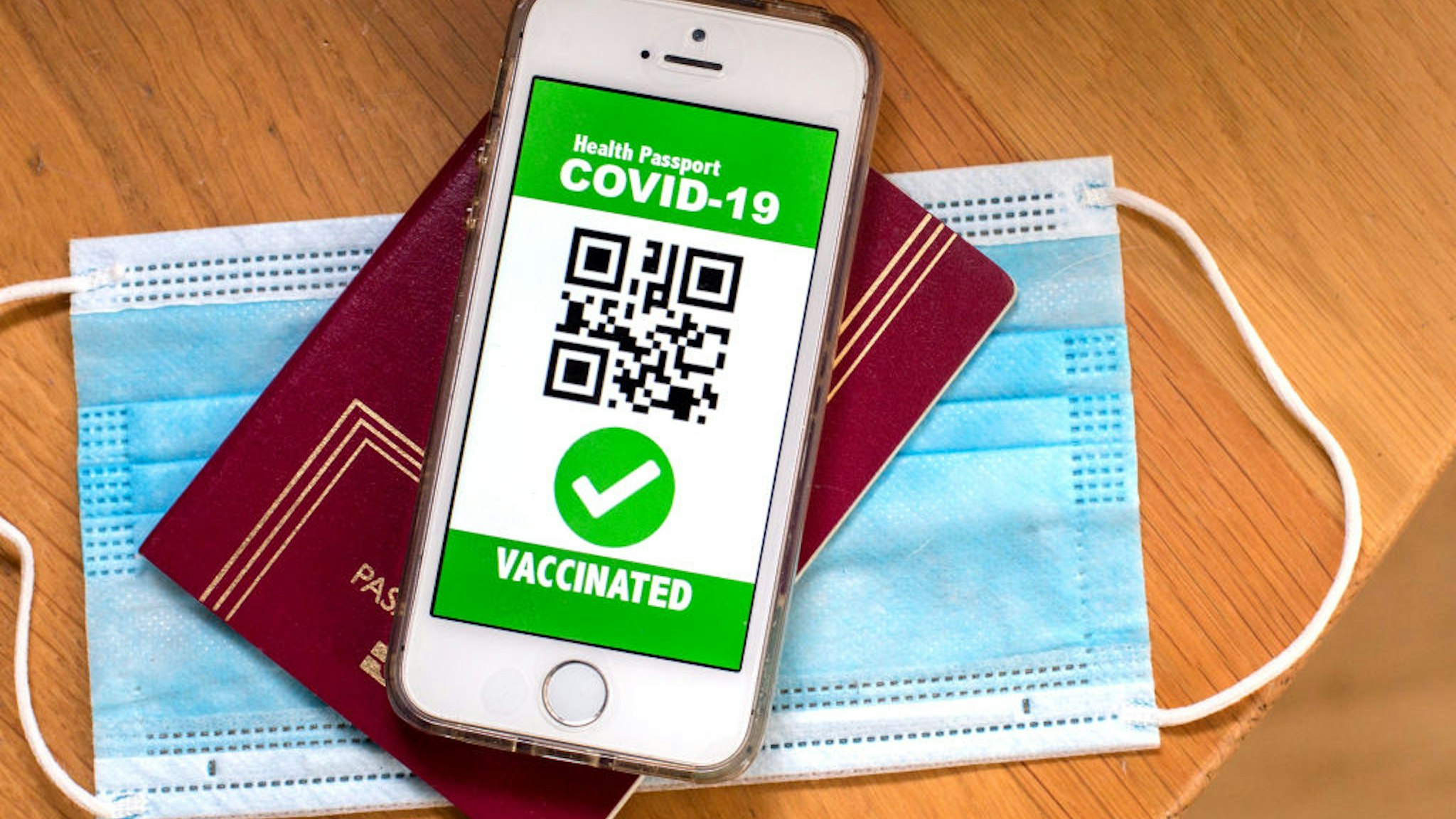 SPAIN - 2021/04/09: In this photo illustration a symbolic COVID-19 health passport seen displayed on a smartphone screen on top of a passport and a protective facemask. (Photo Illustration by Thiago Prudencio/SOPA Images/LightRocket via Getty Images)