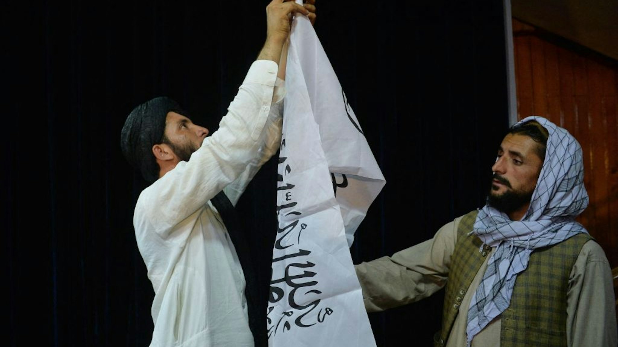 Men adjust the Taliban flag before the arrival of Taliban spokesperson Zabihullah Mujahid (unseen) to address the first press conference in Kabul on August 17, 2021 following the Taliban stunning takeover of Afghanistan. (Photo by Hoshang Hashimi / AFP) (Photo by HOSHANG HASHIMI/AFP via Getty Images)