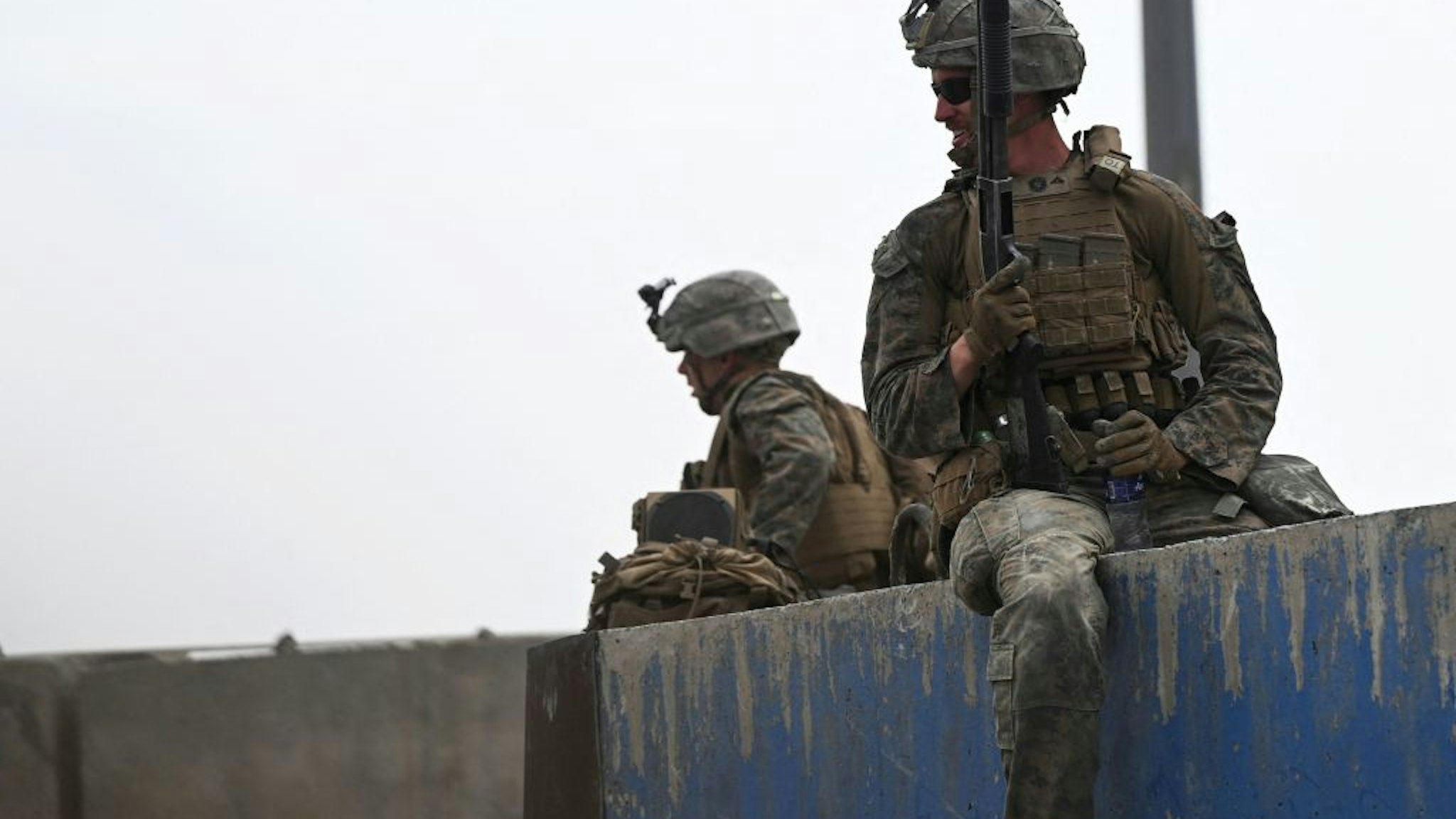 US soldiers sit on a wall as Afghans gather on a roadside near the military part of the airport in Kabul on August 20, 2021, hoping to flee from the country after the Taliban's military takeover of Afghanistan. (Photo by Wakil KOHSAR / AFP) (Photo by WAKIL KOHSAR/AFP via Getty Images)