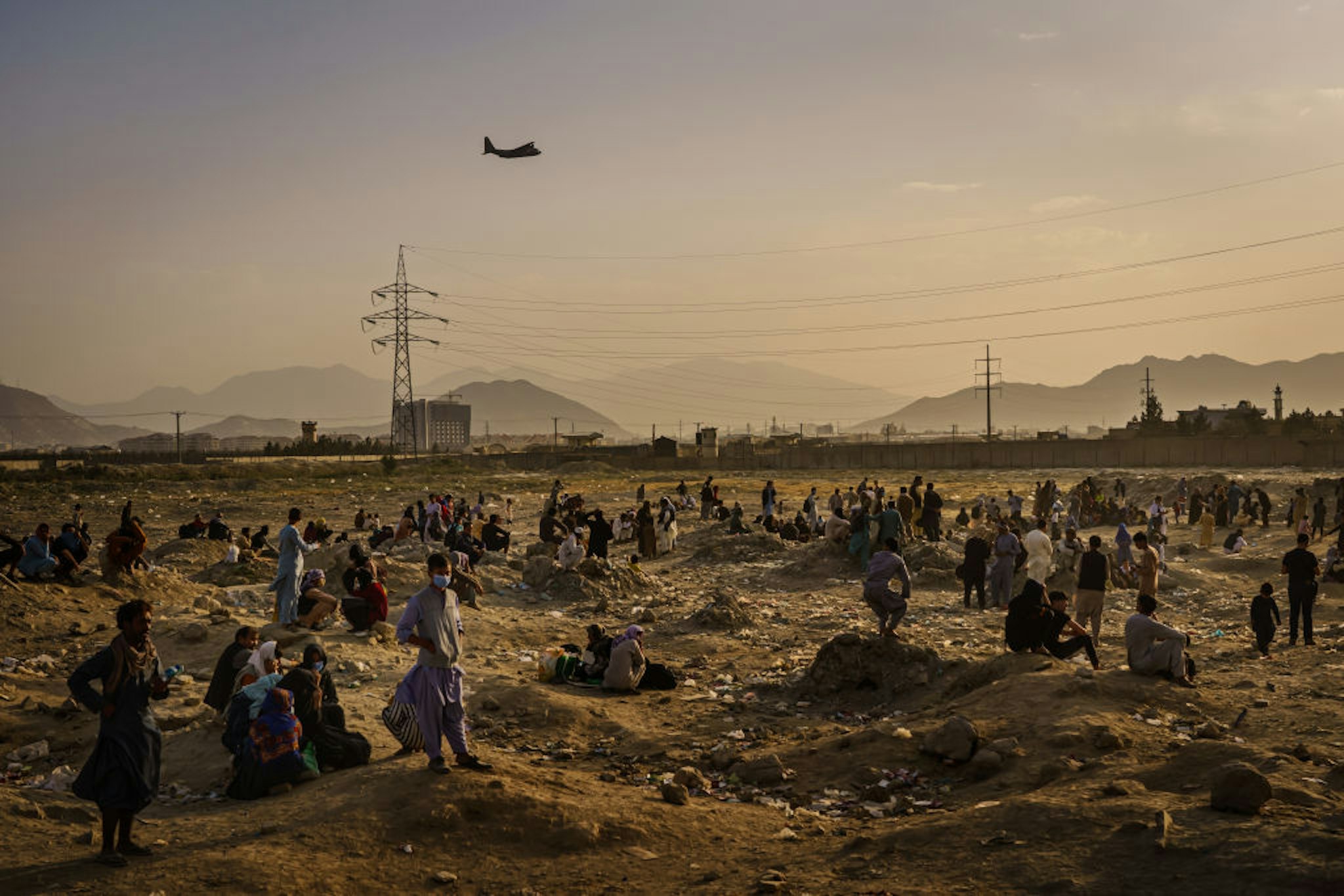 KABUL, AFGHANISTAN -- AUGUST 23, 2021: A military transport plane launches off while Afghans who cannot get into the airport to evacuate, watch and wonder while stranded outside, in Kabul, Afghanistan, Monday, Aug. 23, 2021.