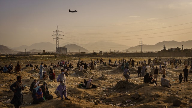 KABUL, AFGHANISTAN -- AUGUST 23, 2021: A military transport plane launches off while Afghans who cannot get into the airport to evacuate, watch and wonder while stranded outside, in Kabul, Afghanistan, Monday, Aug. 23, 2021.