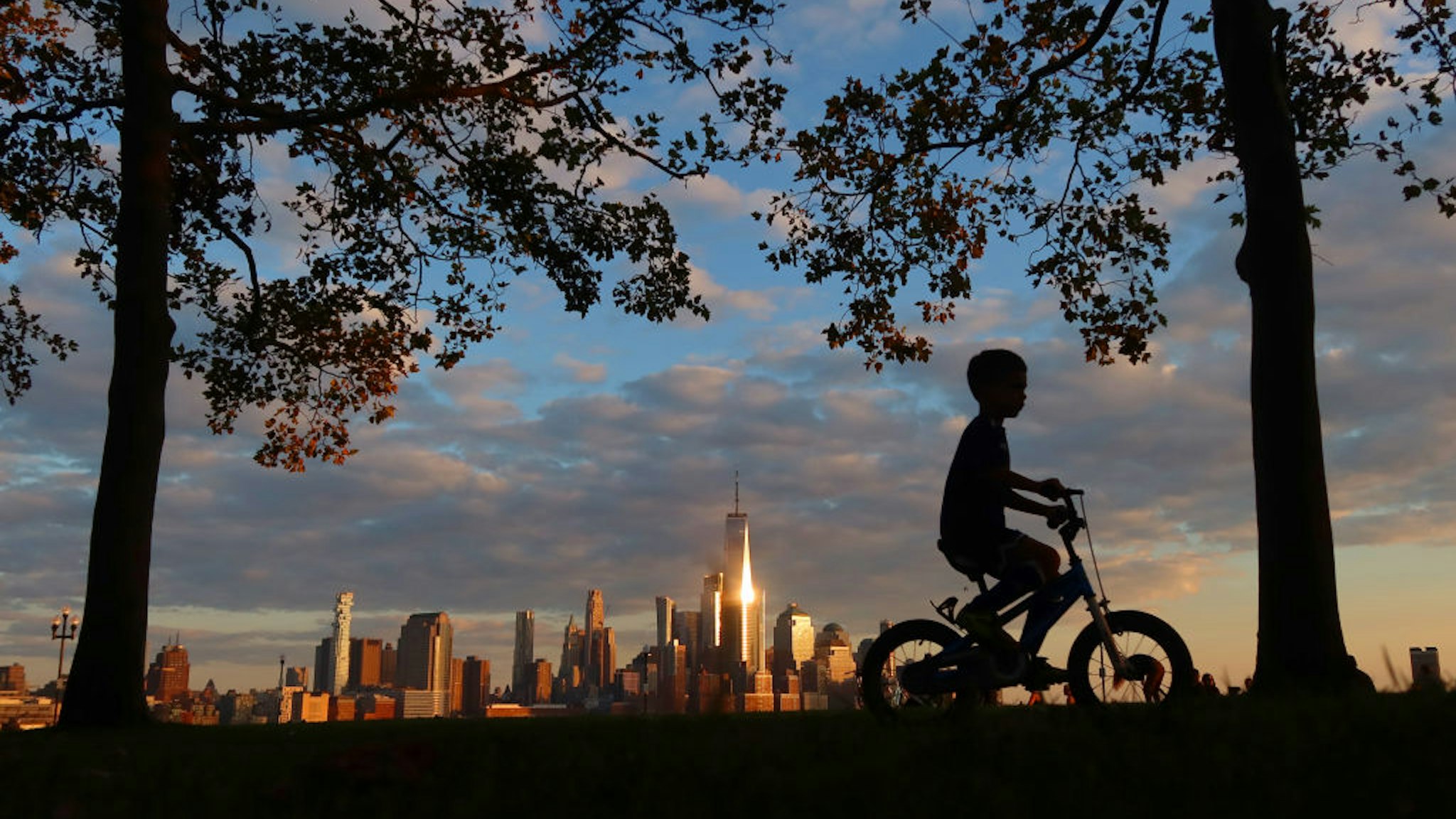 HOBOKEN, NJ - OCTOBER 5: A child rides his bicycle through the park on Pier A as the sun sets on lower Manhattan and One World Trade Center in New York City on October 5, 2020 in Hoboken, New Jersey. (