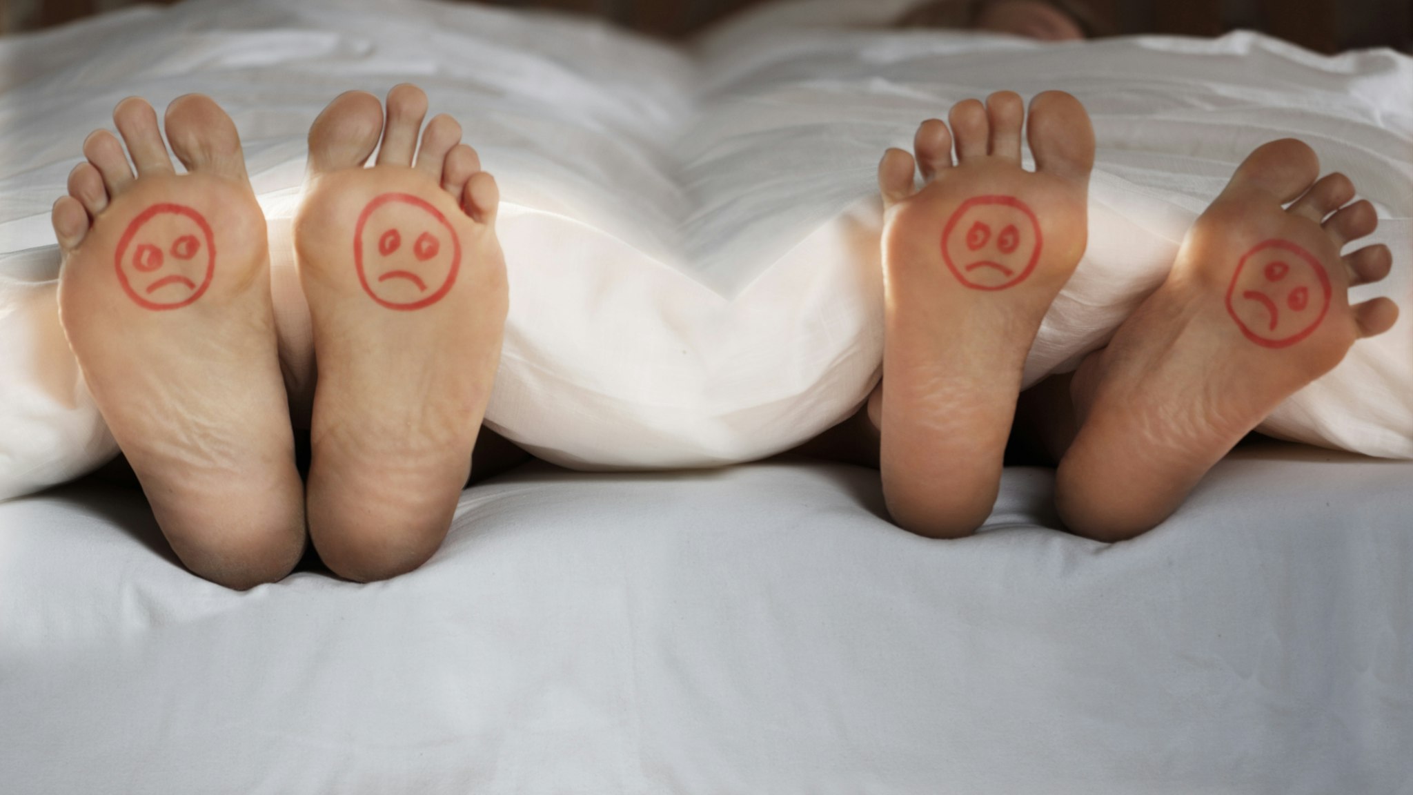 Feet at end of bed with sad faces drawn on - stock photo