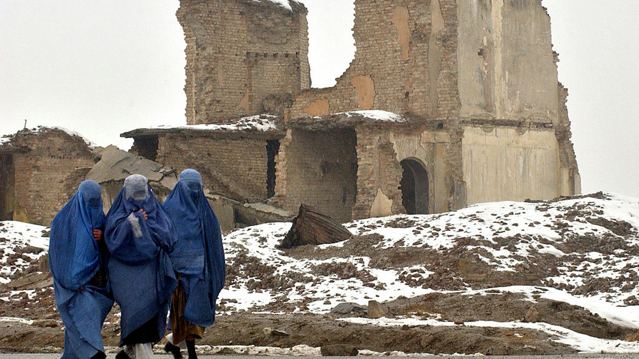 Kabul, AFGHANISTAN: Burqa clad Afghan women walk past a destroyed building in Kabul, 30 January 2006. +The United States has been Afghanistan's biggest donor since leading the war that toppled the Taliban four years ago but it now wants others to carry more of the "burden", US and European officials say.Bargaining over sharing the financial aid on which the country will be dependent for a while yet has intensified in the past months and will be taken up at the London conference on Afghanistan starting 31 January.The United States has disbursed close to five billion USD in the destitute country since 2001. AFP PHOTO/SHAH Marai (Photo credit should read SHAH MARAI/AFP via Getty Images)