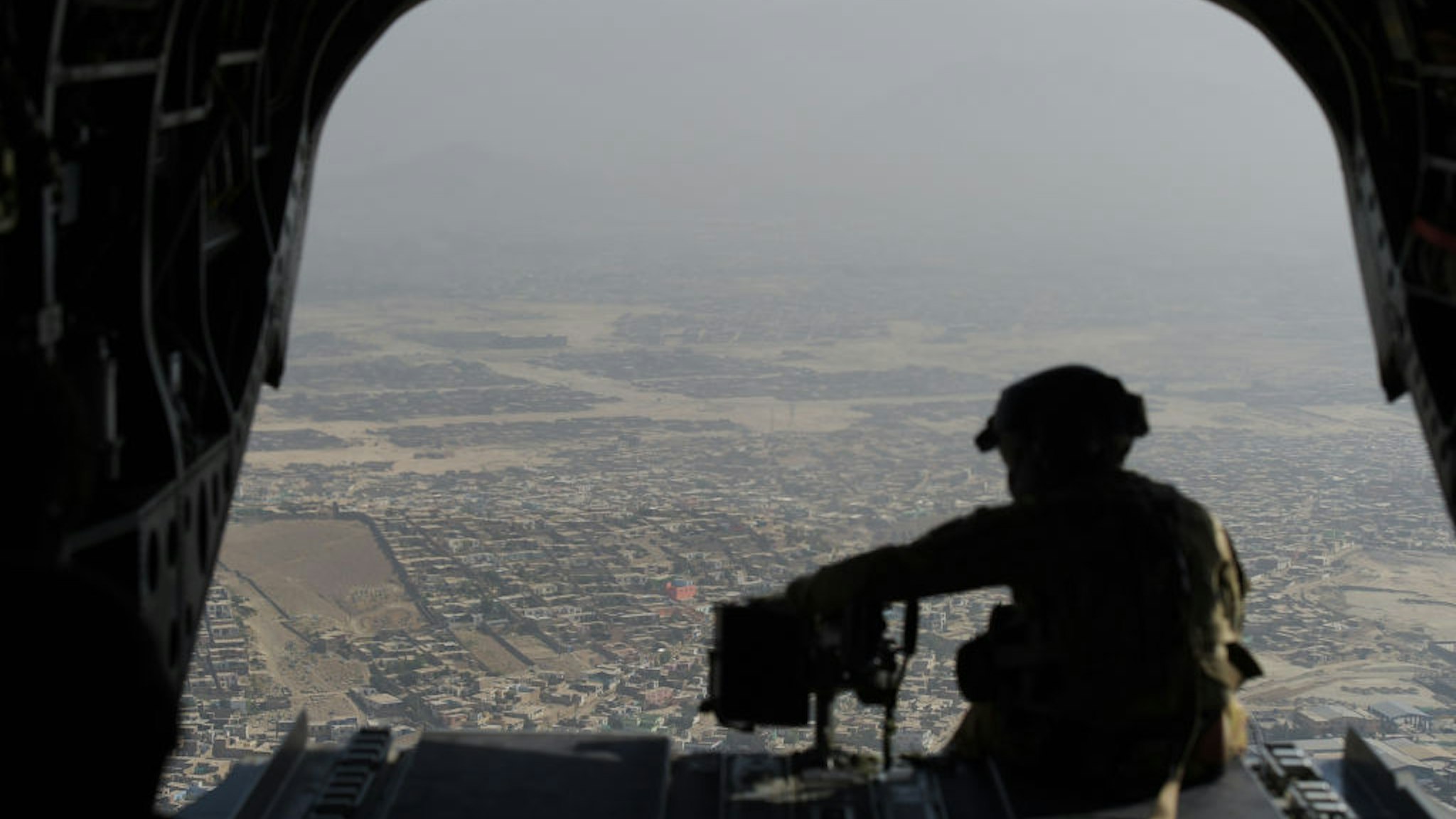In this photograph taken on August 10, 2017, a US soldier sits in the rear of Chinook helicopter while flying over Kabul. Fresh recruits to Afghanistan's elite special operations forces will soon be on the frontline of the war against a resurgent Taliban -- a battle US President Donald Trump has vowed "to win" by putting more American boots on the ground indefinitely. Camp Morehead, a former Soviet base near Kabul, is one of two training bases where the commandos are drilled by Afghan instructors in a programme overseen by US-led international forces. / AFP PHOTO / SHAH MARAI / TO GO WITH: Afghanistan-army-conflict, FOCUS by Anne CHAON (Photo credit should read SHAH MARAI/AFP via Getty Images)