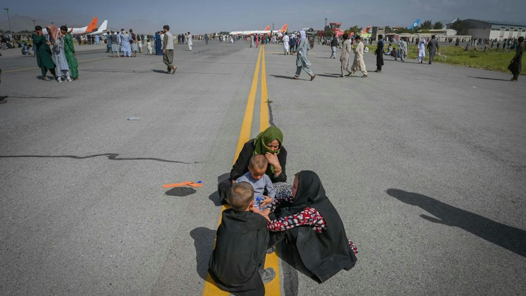 Afghan people sit along the tarmac as they wait to leave the Kabul airport in Kabul on August 16, 2021, after a stunningly swift end to Afghanistan's 20-year war, as thousands of people mobbed the city's airport trying to flee the group's feared hardline brand of Islamist rule.