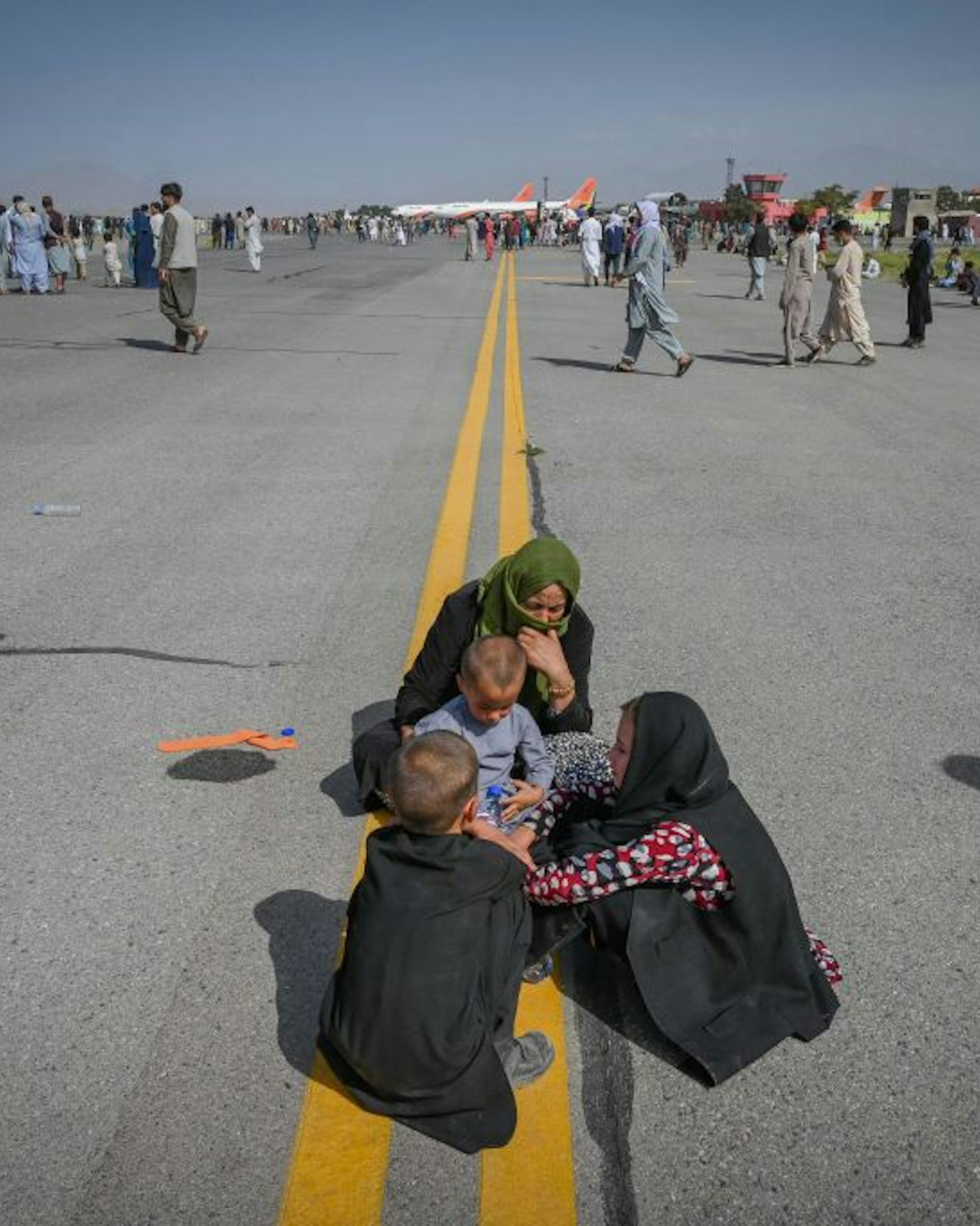 Afghan people sit along the tarmac as they wait to leave the Kabul airport in Kabul on August 16, 2021, after a stunningly swift end to Afghanistan's 20-year war, as thousands of people mobbed the city's airport trying to flee the group's feared hardline brand of Islamist rule.