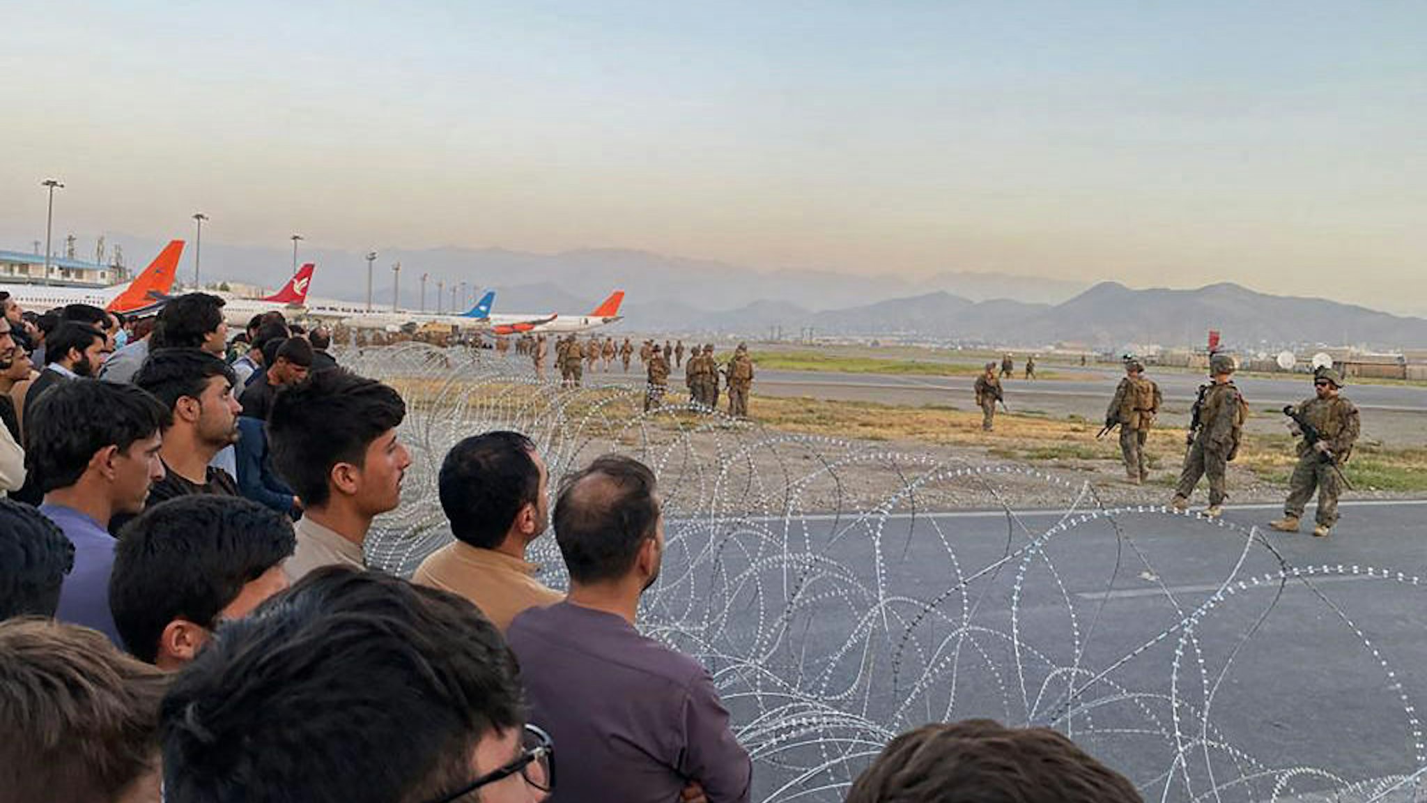 TOPSHOT - Afghans (L) crowd at the airport as US soldiers stand guard in Kabul on August 16, 2021. (Photo by Shakib Rahmani / AFP) (Photo by SHAKIB RAHMANI/AFP via Getty Images)