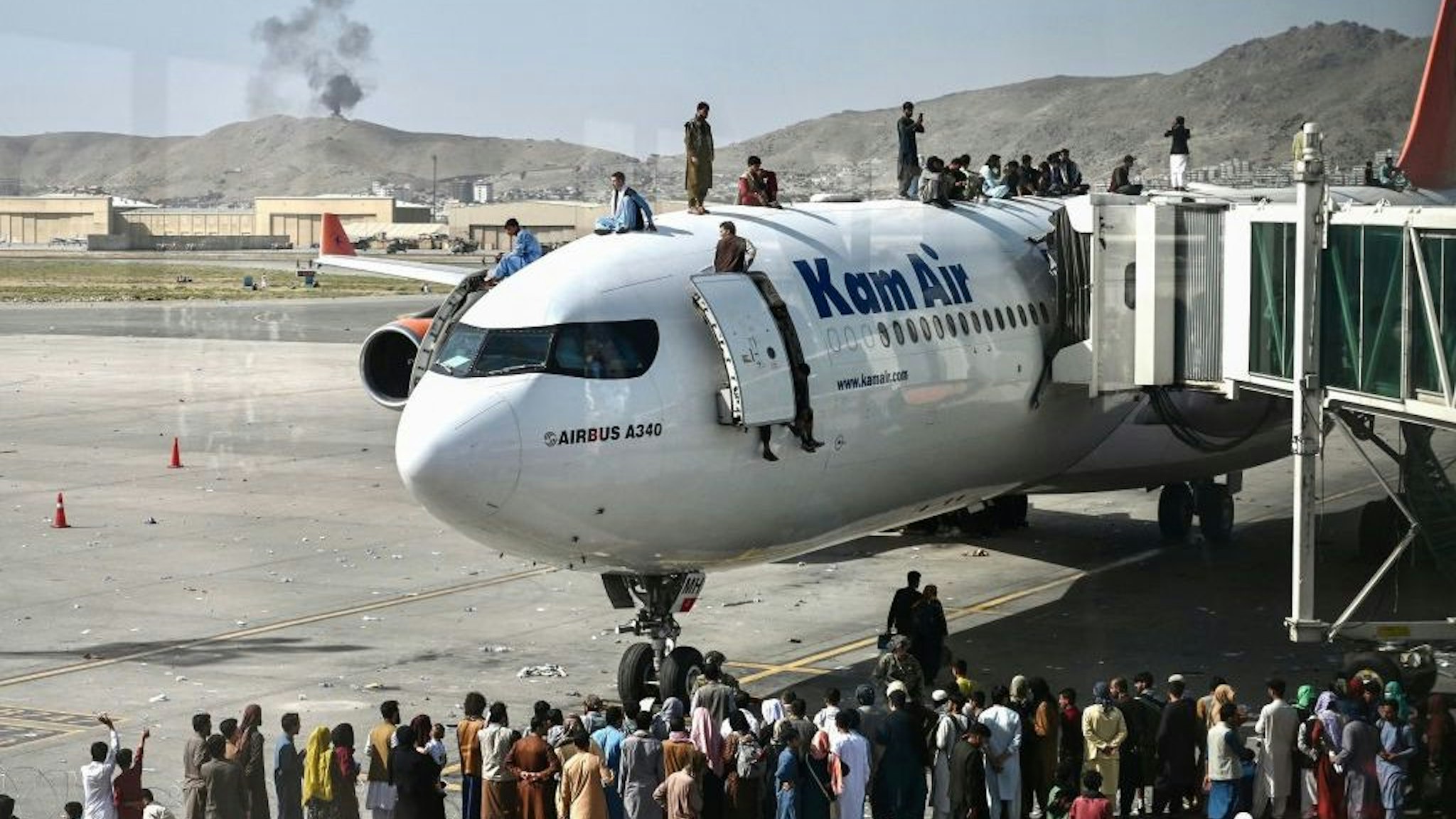 TOPSHOT - Afghan people climb atop a plane as they wait at the Kabul airport in Kabul on August 16, 2021, after a stunningly swift end to Afghanistan's 20-year war, as thousands of people mobbed the city's airport trying to flee the group's feared hardline brand of Islamist rule. (Photo by Wakil Kohsar / AFP) (Photo by WAKIL KOHSAR/AFP via Getty Images)