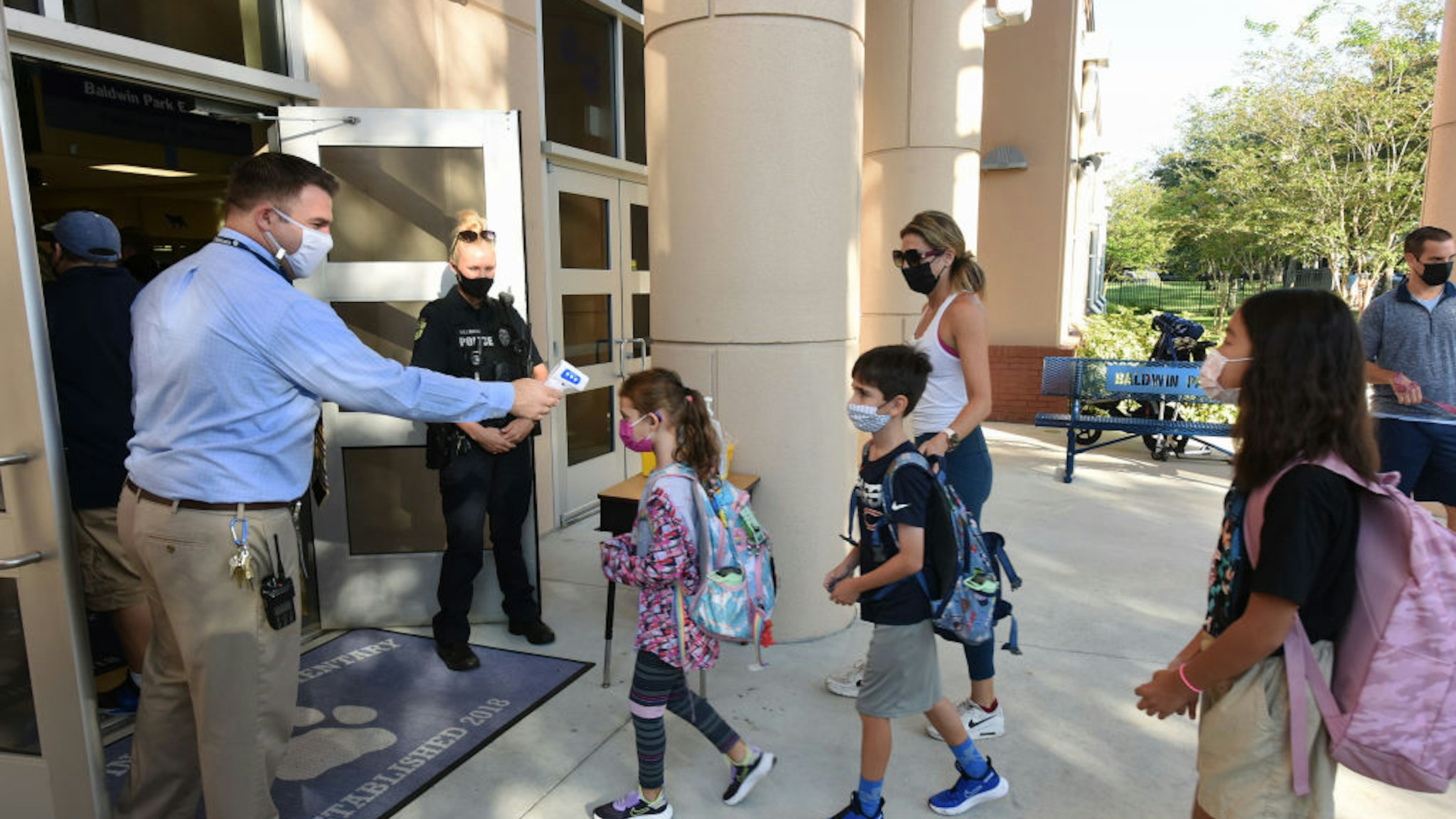 ORLANDO, FLORIDA, UNITED STATES - 2021/08/10: Principal Nathan Hay performs temperature checks on students as they arrive on the first day of classes for the 2021-22 school year at Baldwin Park Elementary School. Due to the current surge in COVID-19 cases in Florida, Orange County public schools have implemented a face mask mandate for students for 30 days unless a parent chooses to opt out of the requirement.